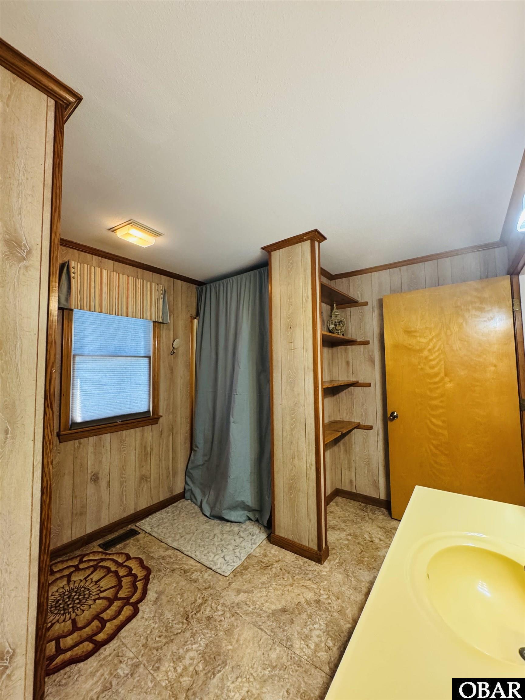 Bathroom with a yellow bathtub, wood-paneled walls, and a curtained shower area.