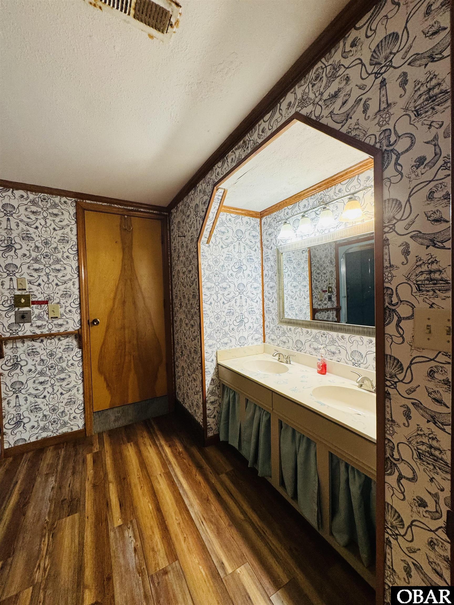 Bathroom with double-sink vanity, large mirror, and nautical-patterned wallpaper.