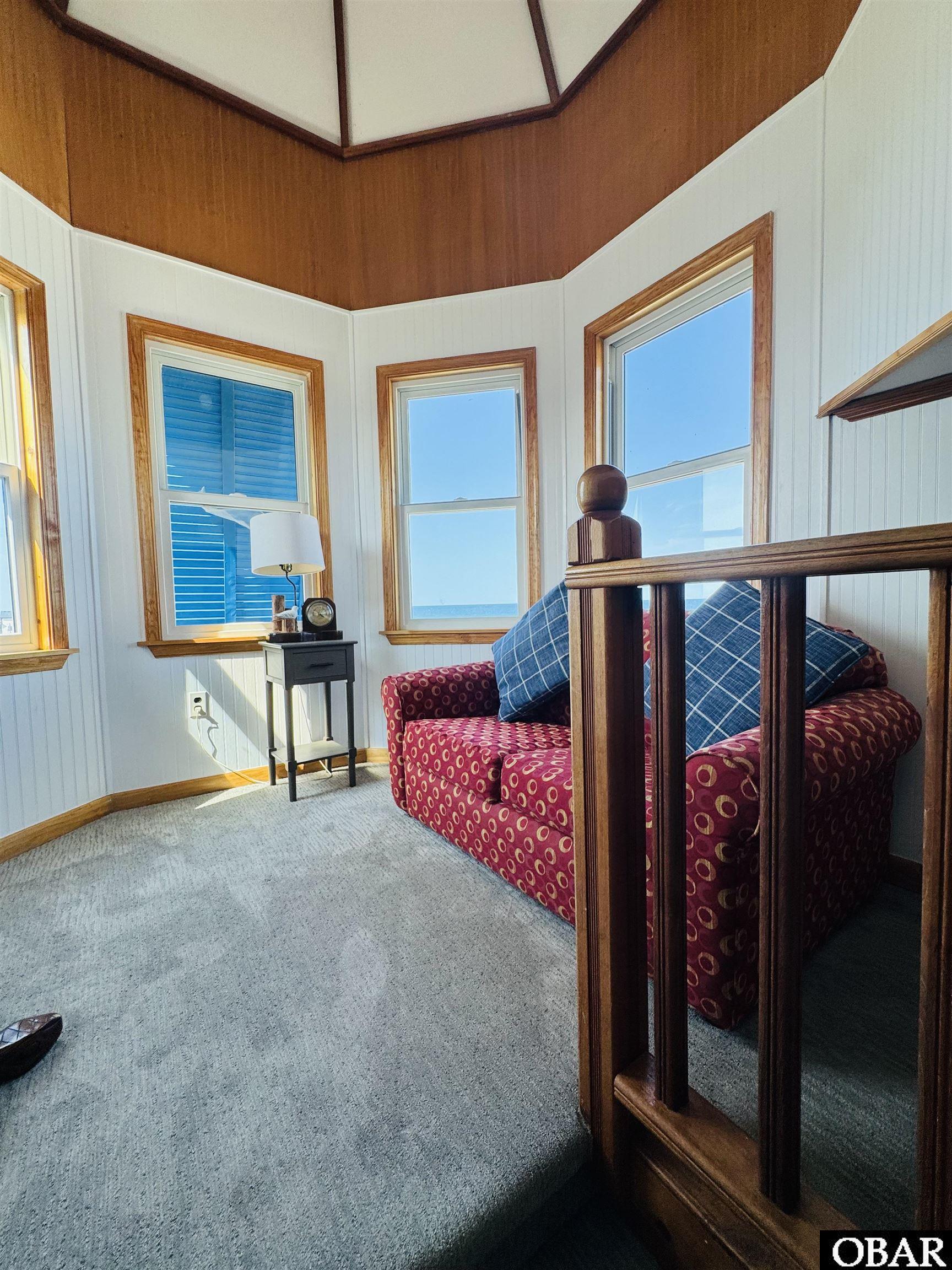 Furnished sitting area with a patterned loveseat and ocean views through tall windows.