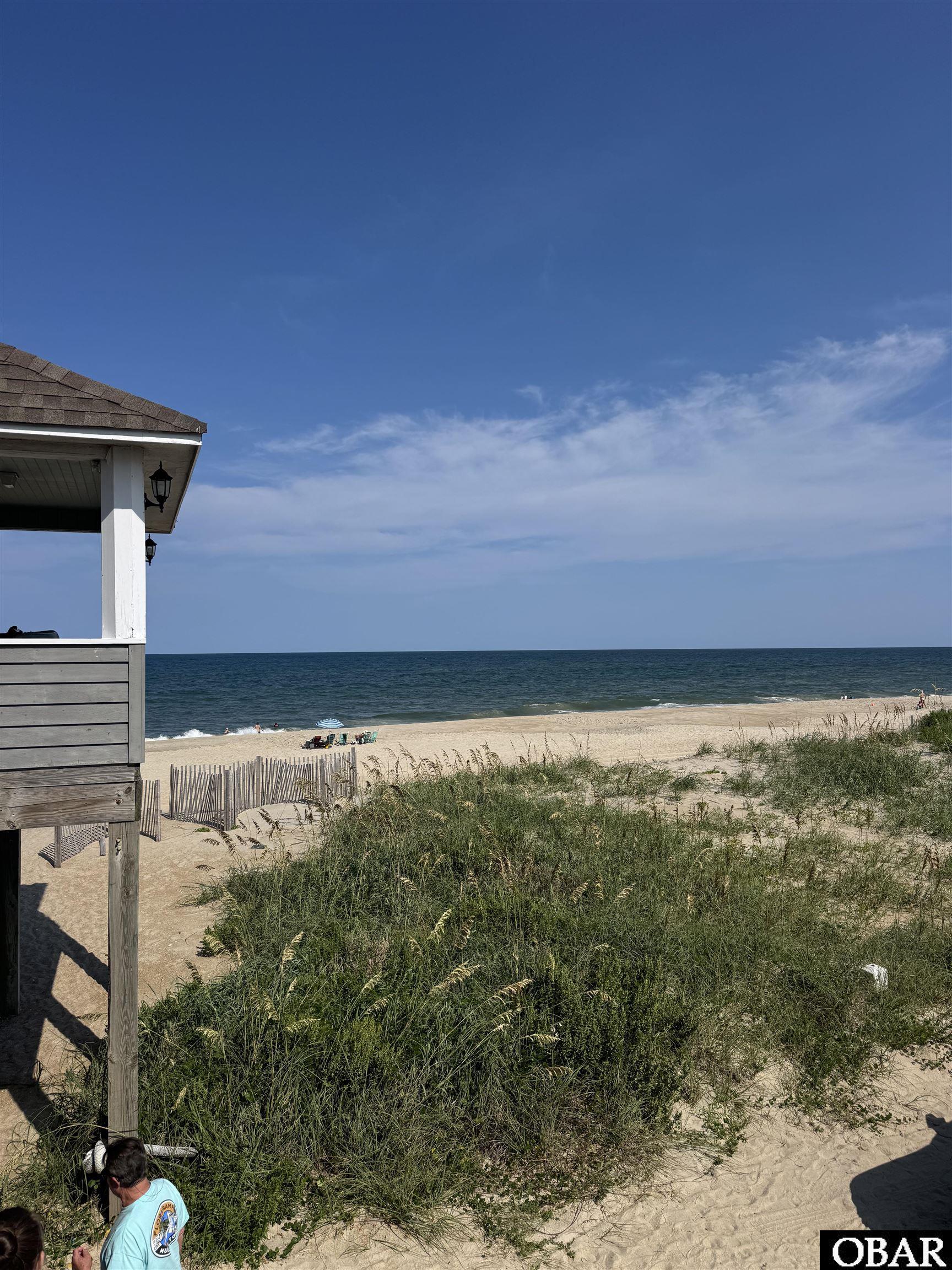 Sandy beach and ocean beyond dune grass, with a beach house at the left edge.