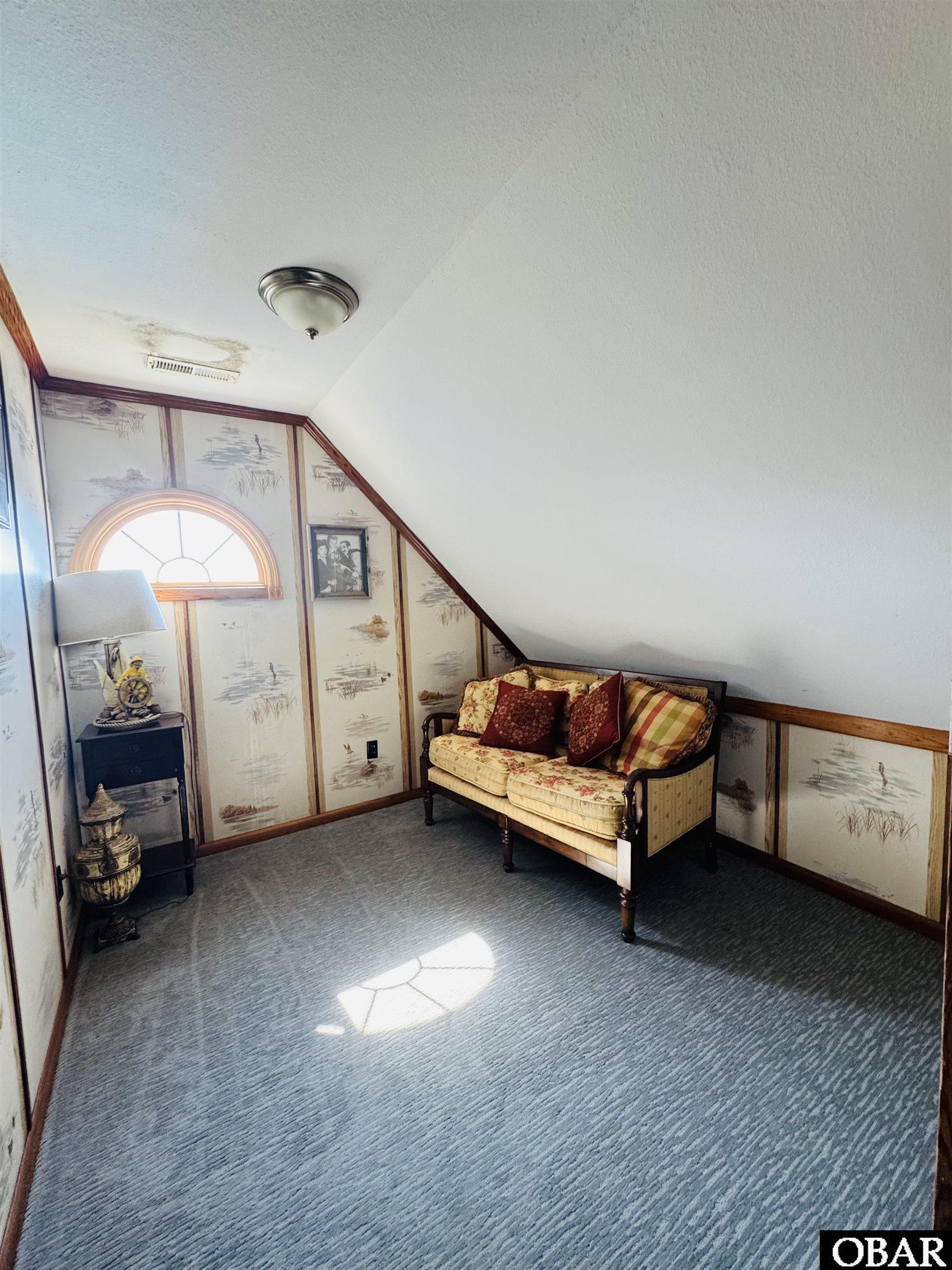 Furnished sitting nook with a floral loveseat, arched window, patterned walls, and sloped ceiling.