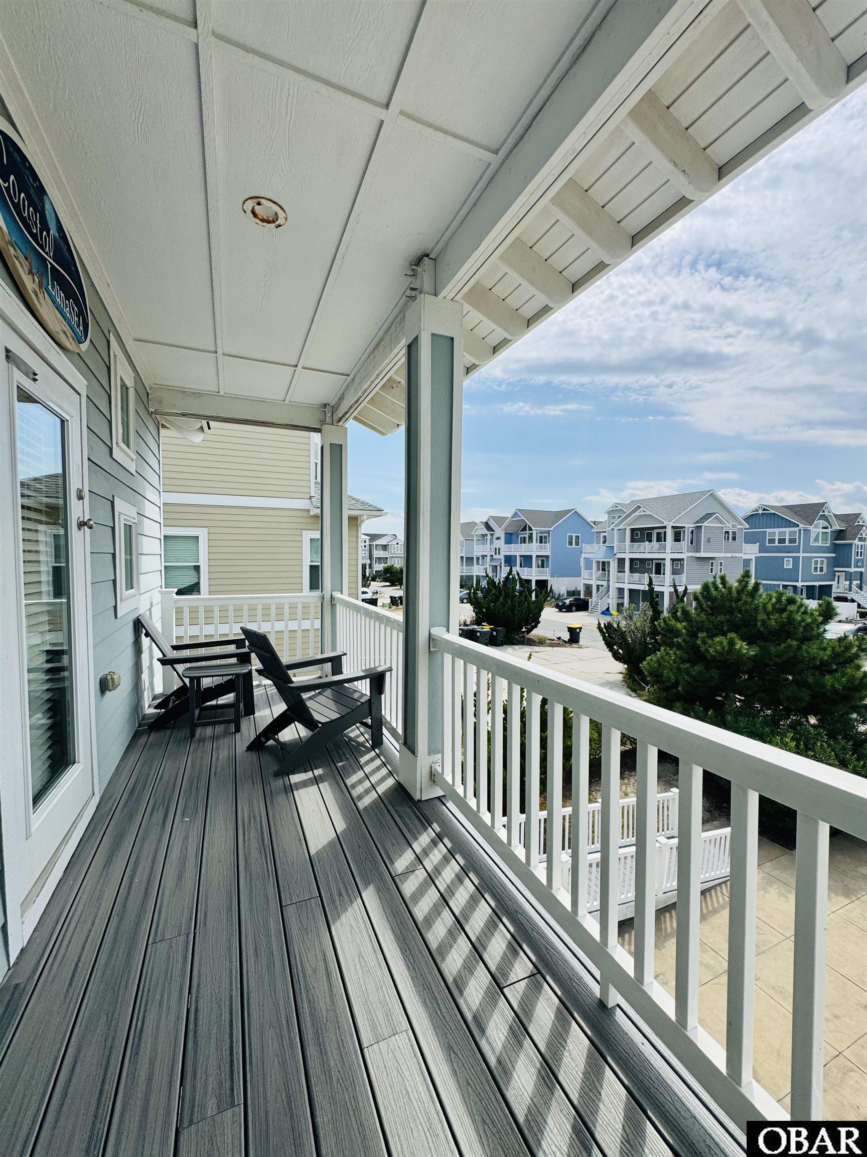 Covered balcony with two black chairs overlooking neighboring coastal-style homes.