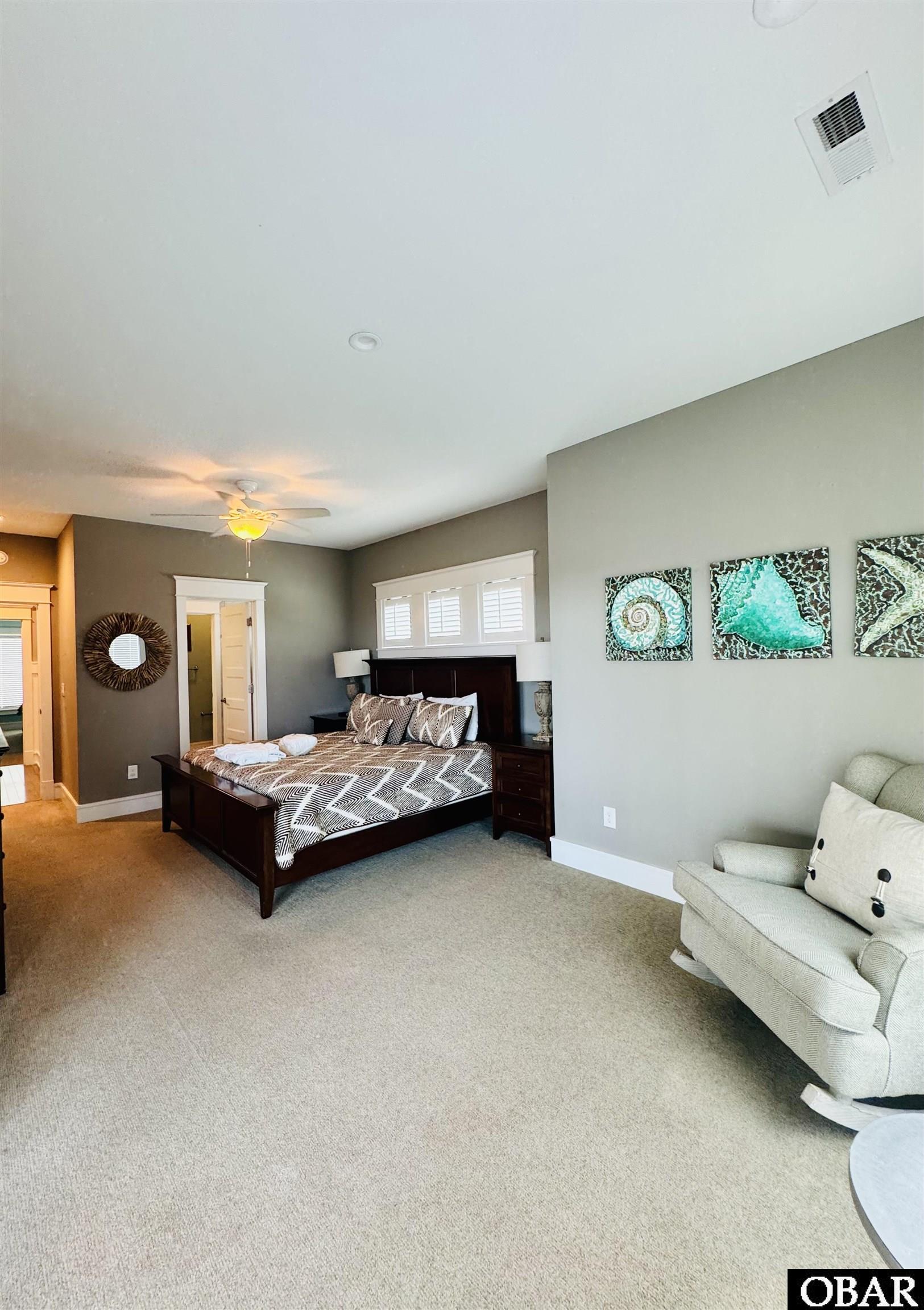 Bedroom with a dark wood king bed, patterned bedding, and a pale loveseat beneath turquoise shell artwork.