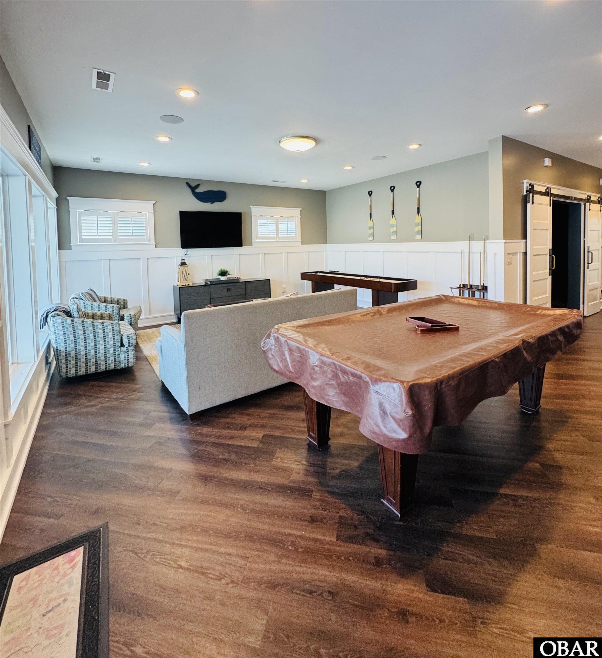 Game room with a pool table, shuffleboard table, and seating area with a television.