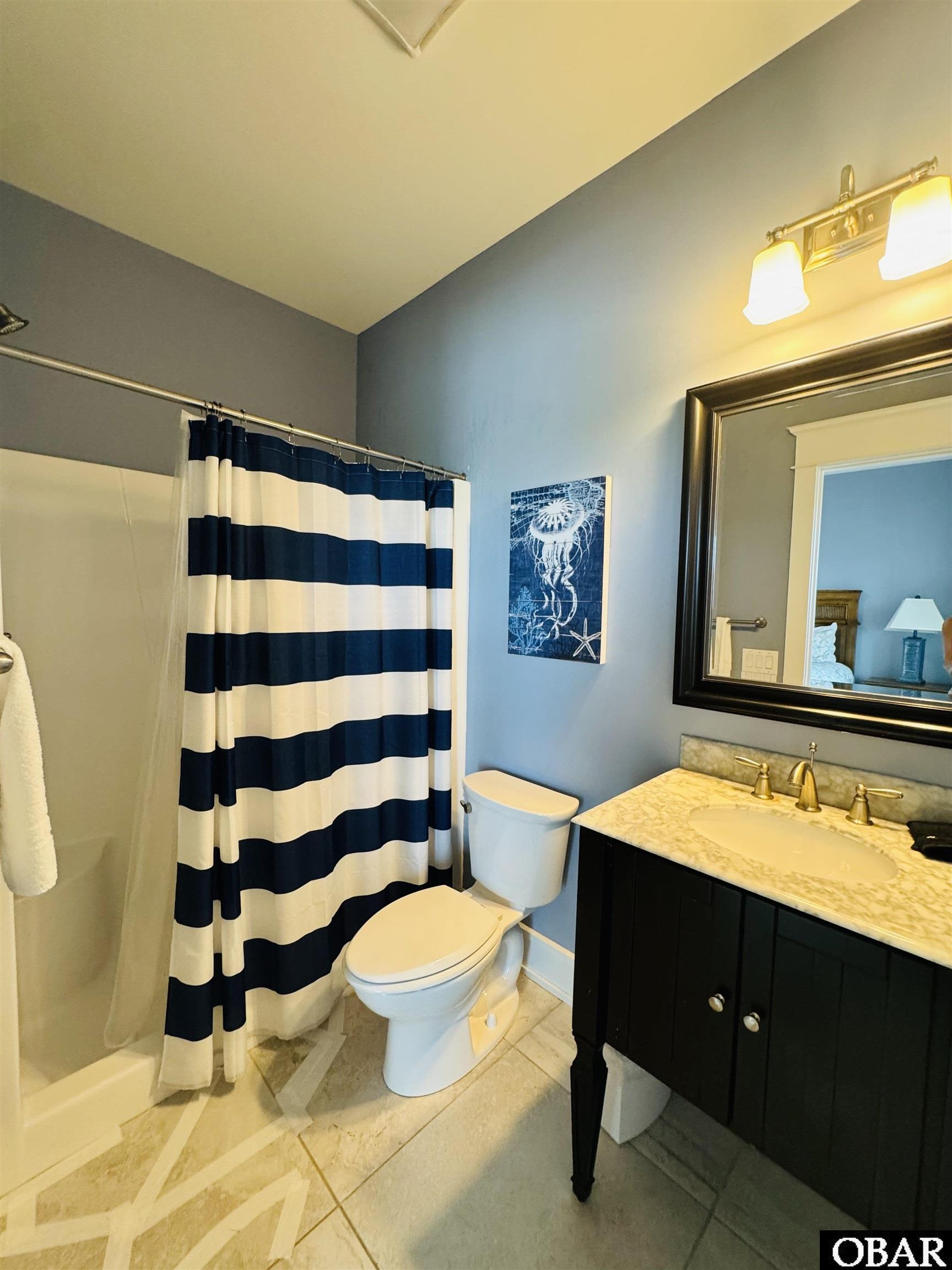 Bathroom with striped shower curtain, dark vanity, marble countertop, and large framed mirror.
