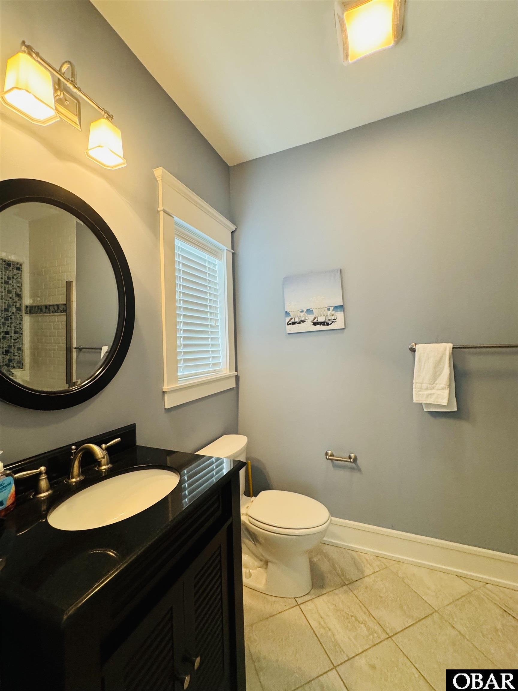 Bathroom with a black vanity, round mirror, toilet, and shuttered window.