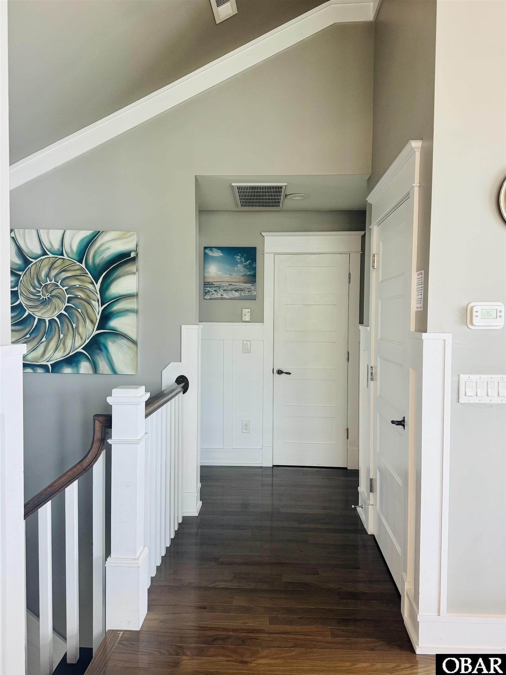 Hallway with dark wood floors, white paneled doors, stair railing, and large teal shell artwork.