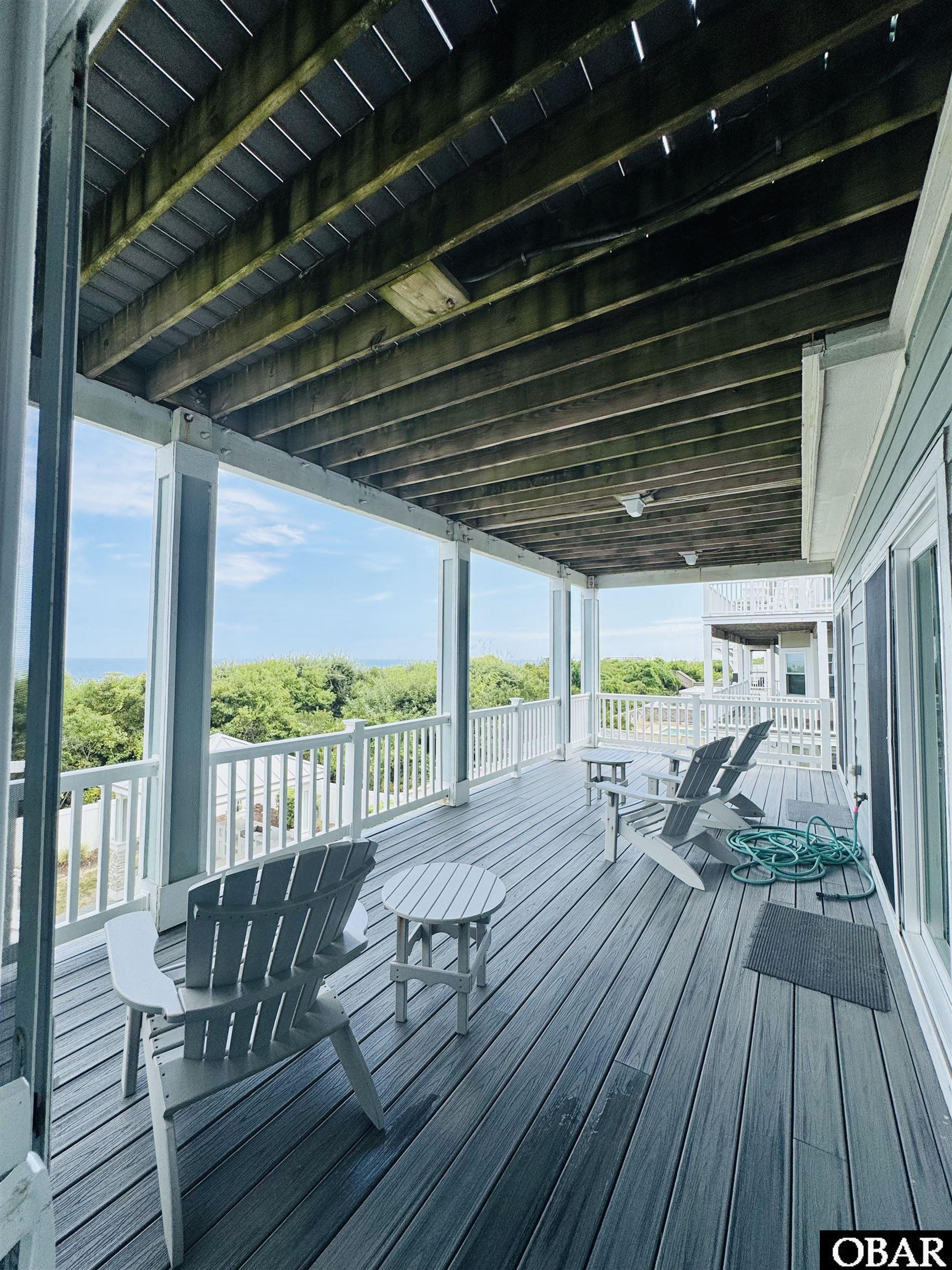 Covered deck with Adirondack chairs and an ocean view beyond coastal vegetation.