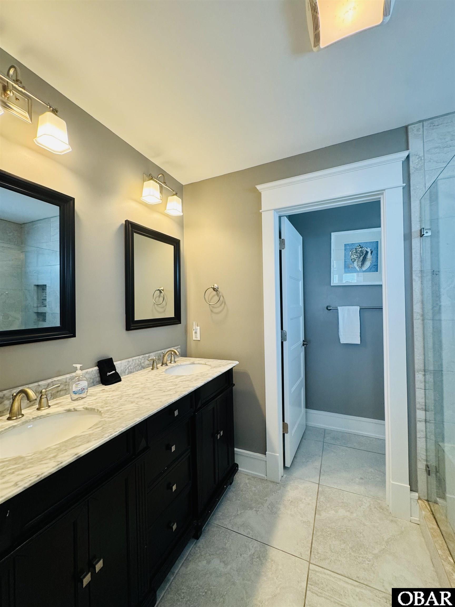Bathroom with a dark double vanity, pale stone countertop, and glass shower.