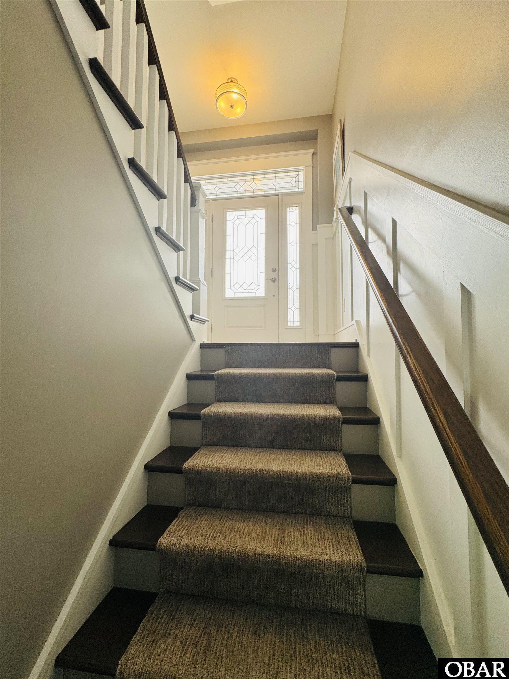 Carpeted staircase with dark wood treads and railing leading to a glass-paneled front door.