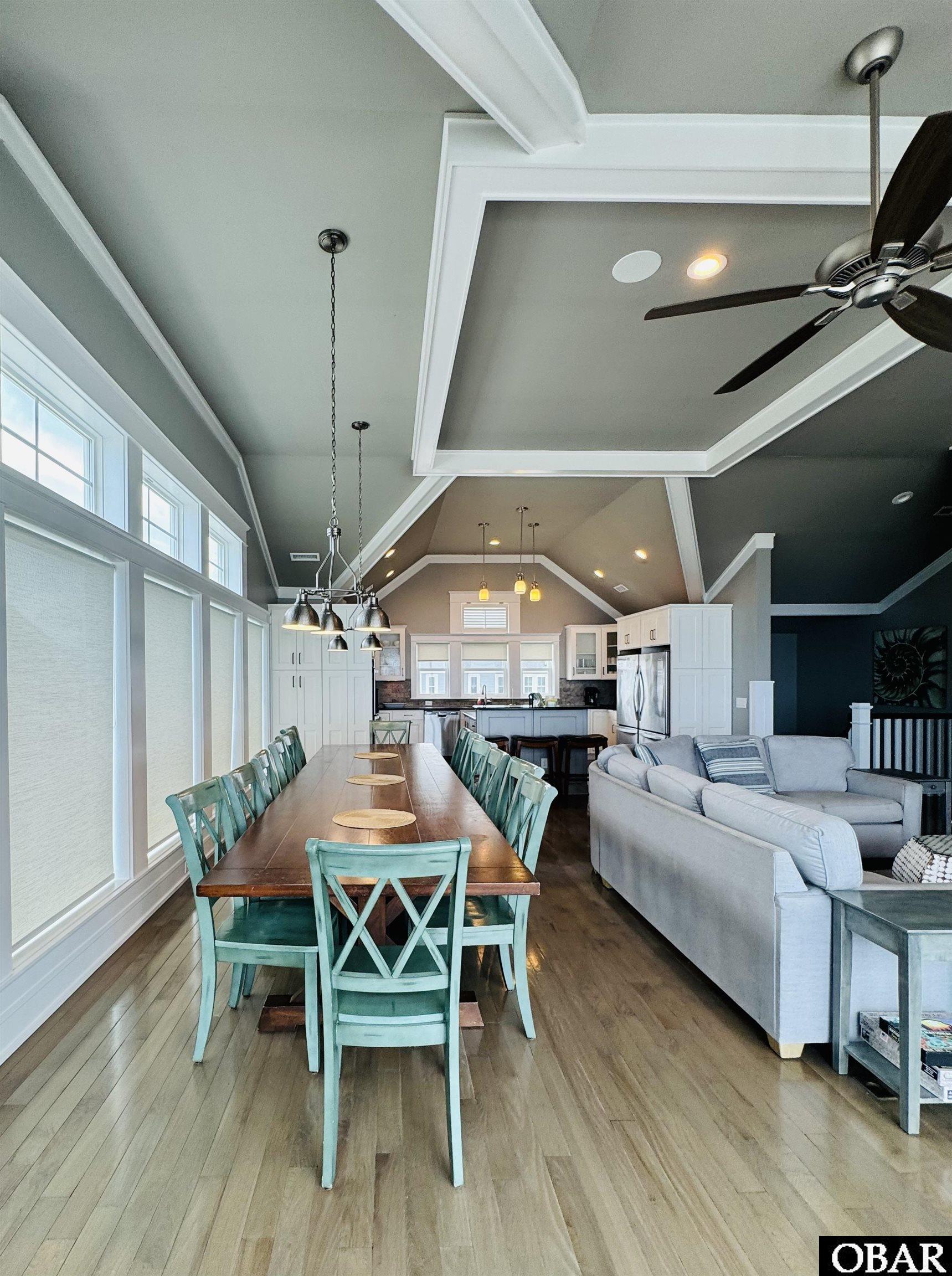 Open-plan dining and living area with turquoise chairs, a gray sectional, and a vaulted ceiling.