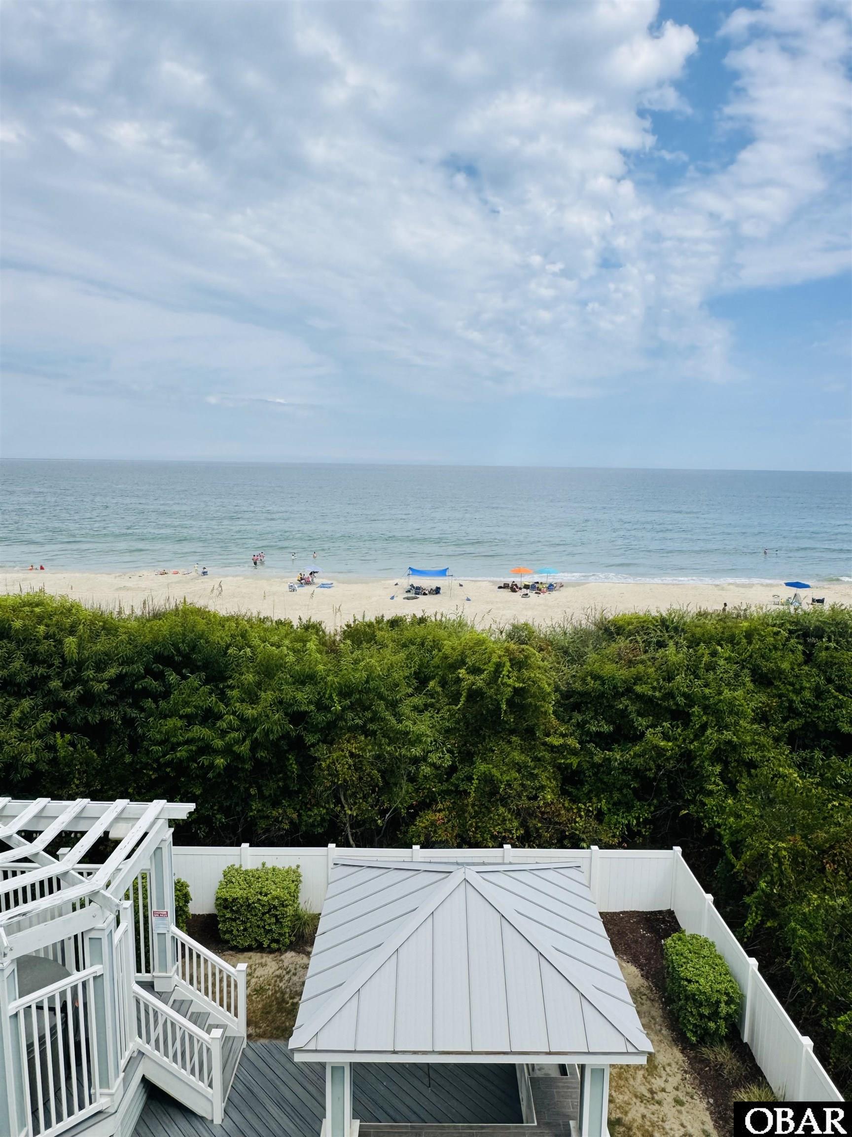 Elevated deck and fenced yard overlook a beach with beachgoers and the ocean.