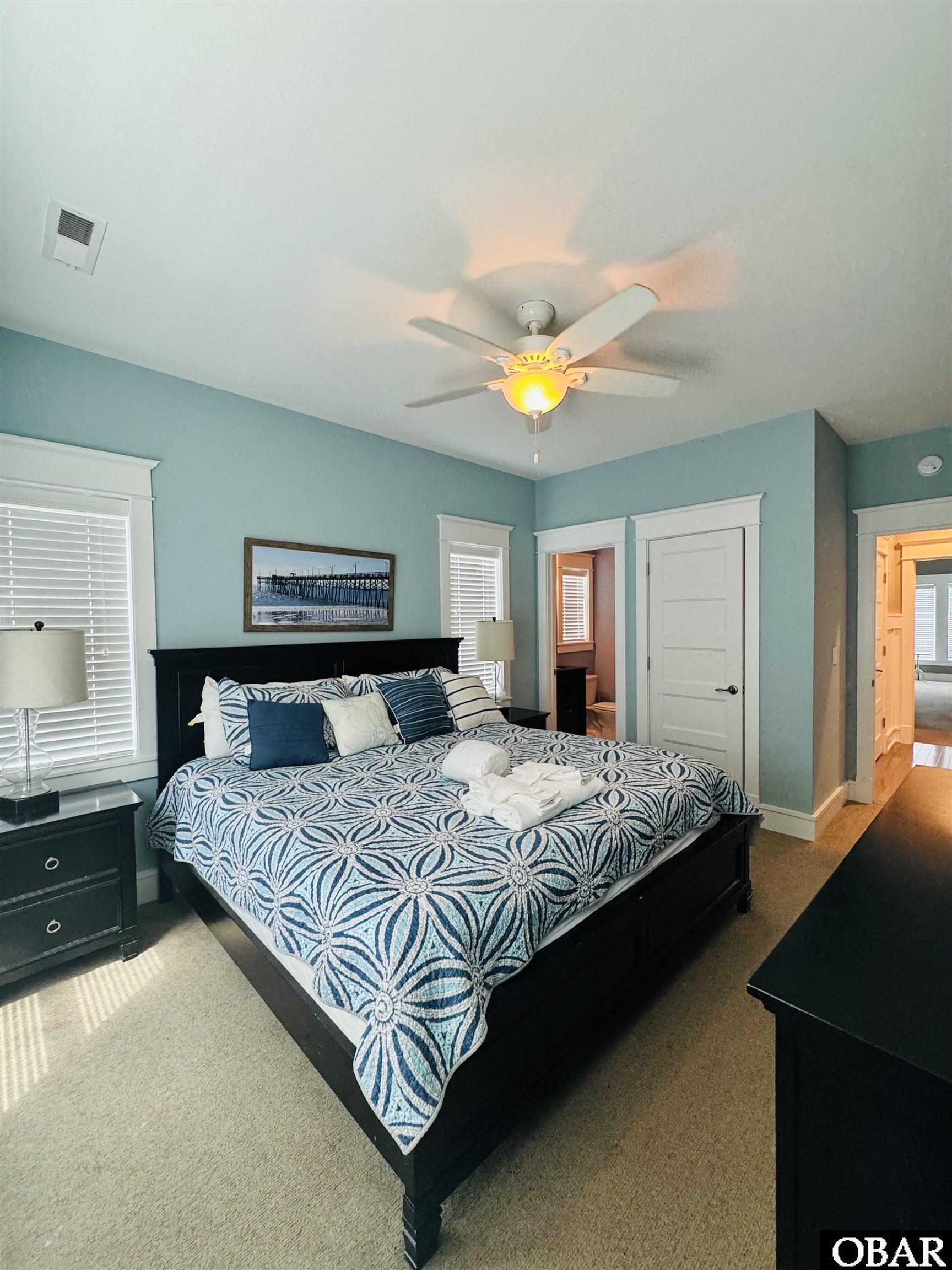 Bedroom with a blue-and-white patterned bedspread, blue walls, and a lit ceiling fan.