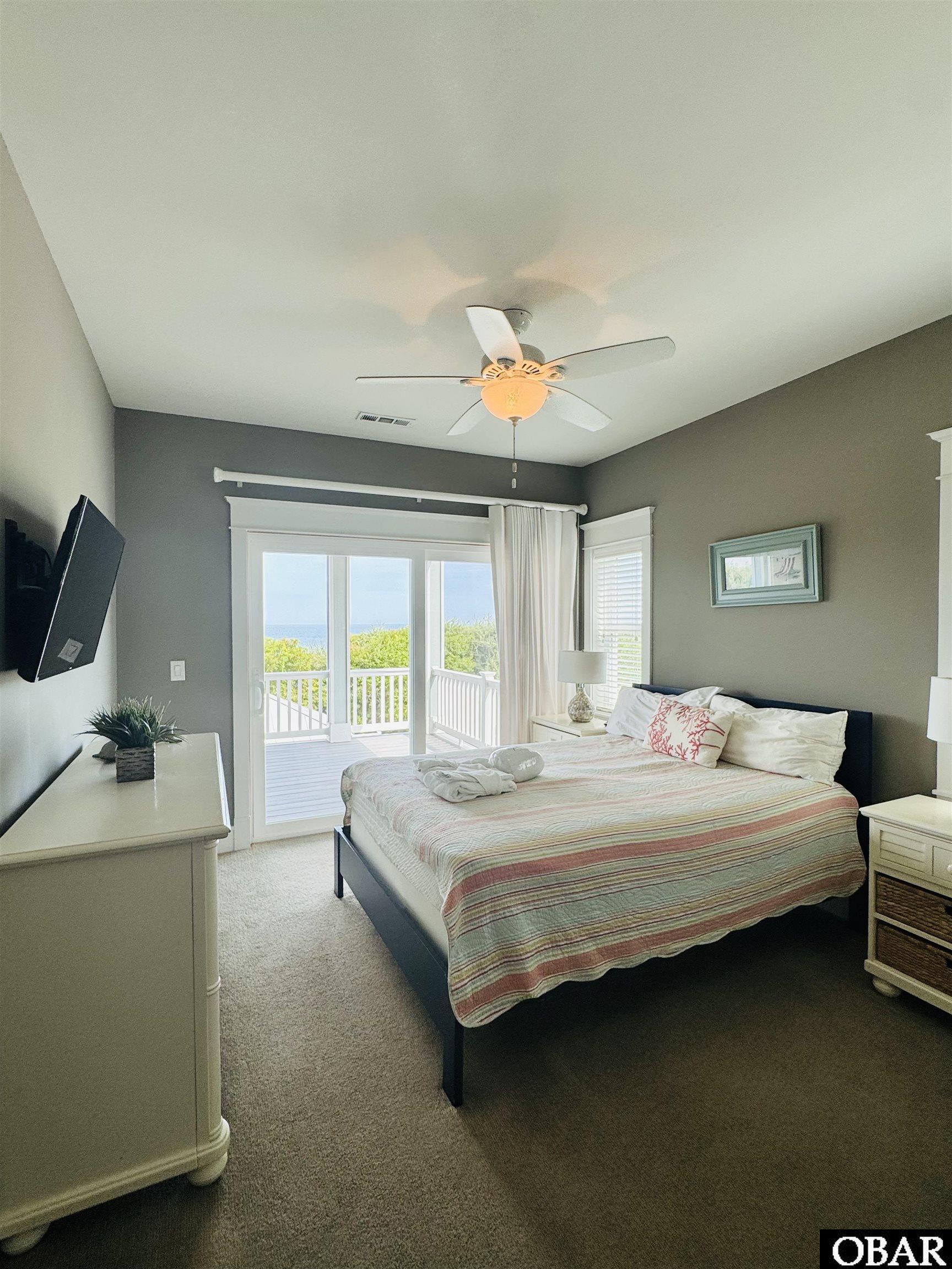Bedroom with a striped bedspread and sliding doors overlooking a deck and ocean.