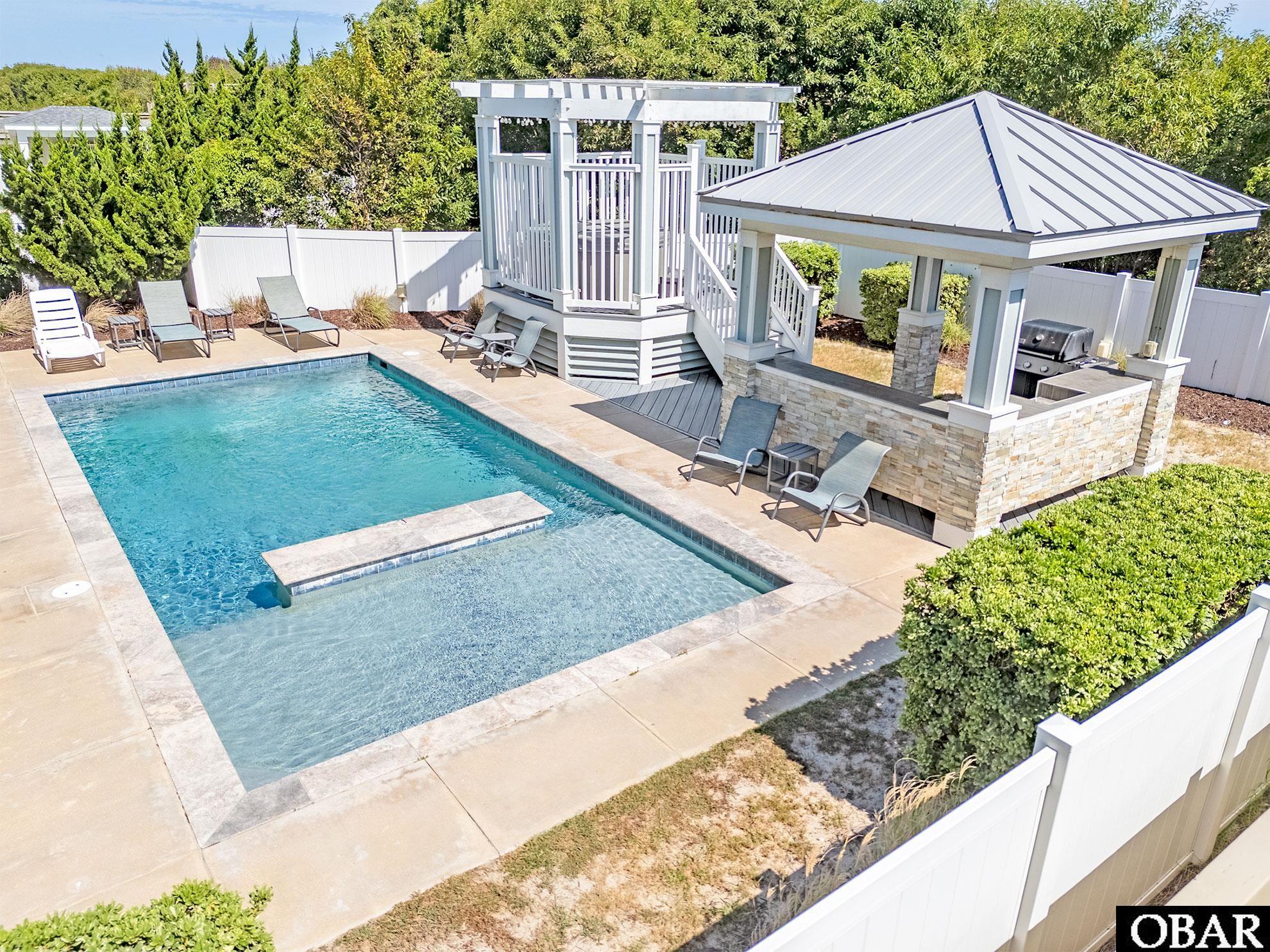 Backyard pool with a shallow ledge, raised pergola, and covered outdoor grill pavilion.