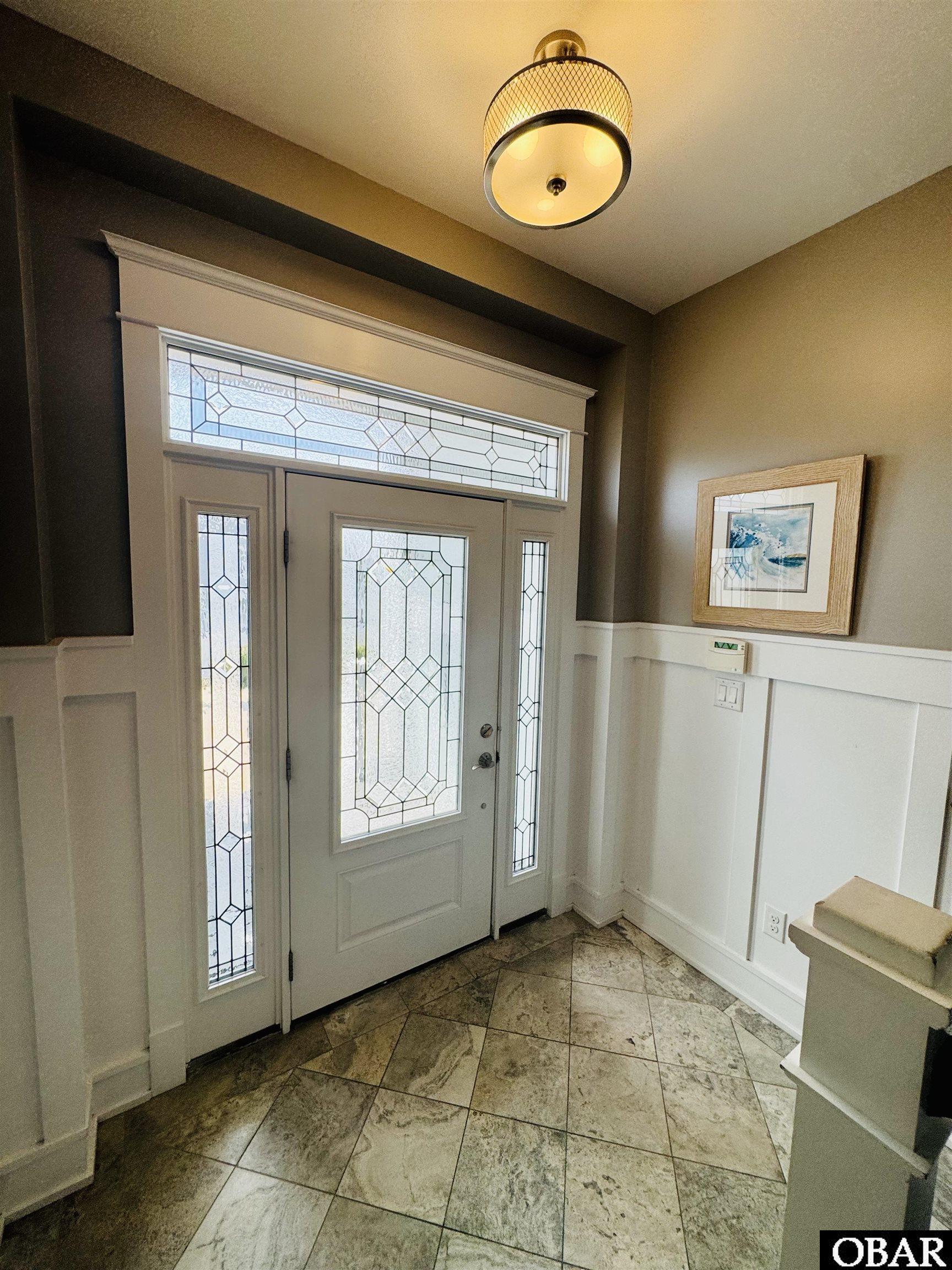 Entry foyer with a decorative glass front door, matching sidelights, and stone tile flooring.