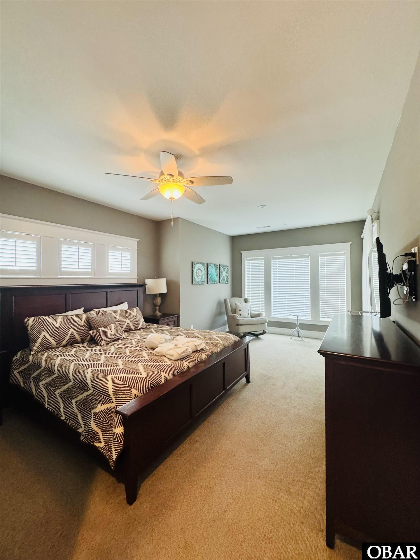 Furnished bedroom with a dark wood bed, geometric bedding, ceiling fan, and shuttered windows.