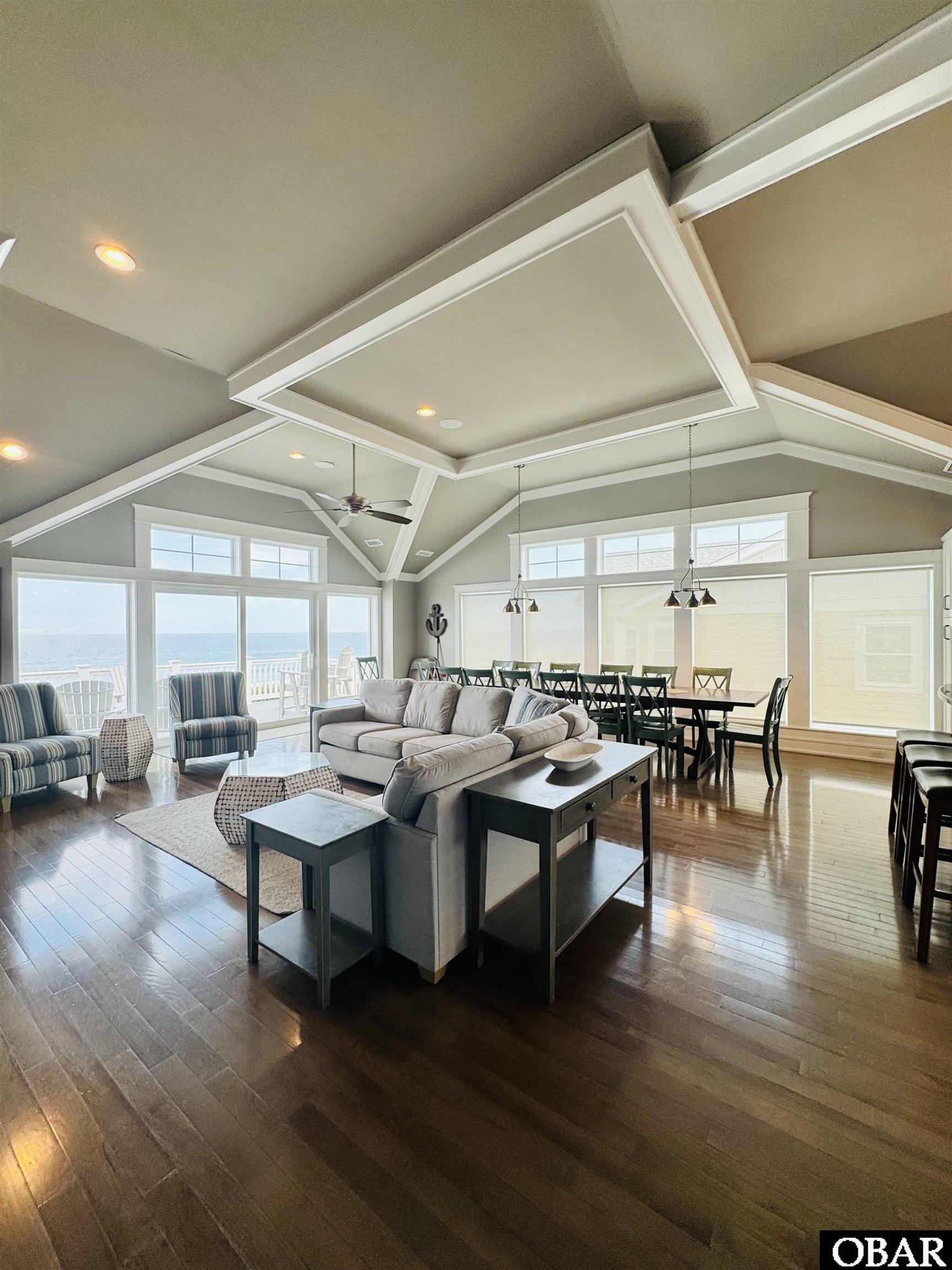 Open-plan living and dining room with vaulted ceilings, dark floors, and ocean views through large windows.