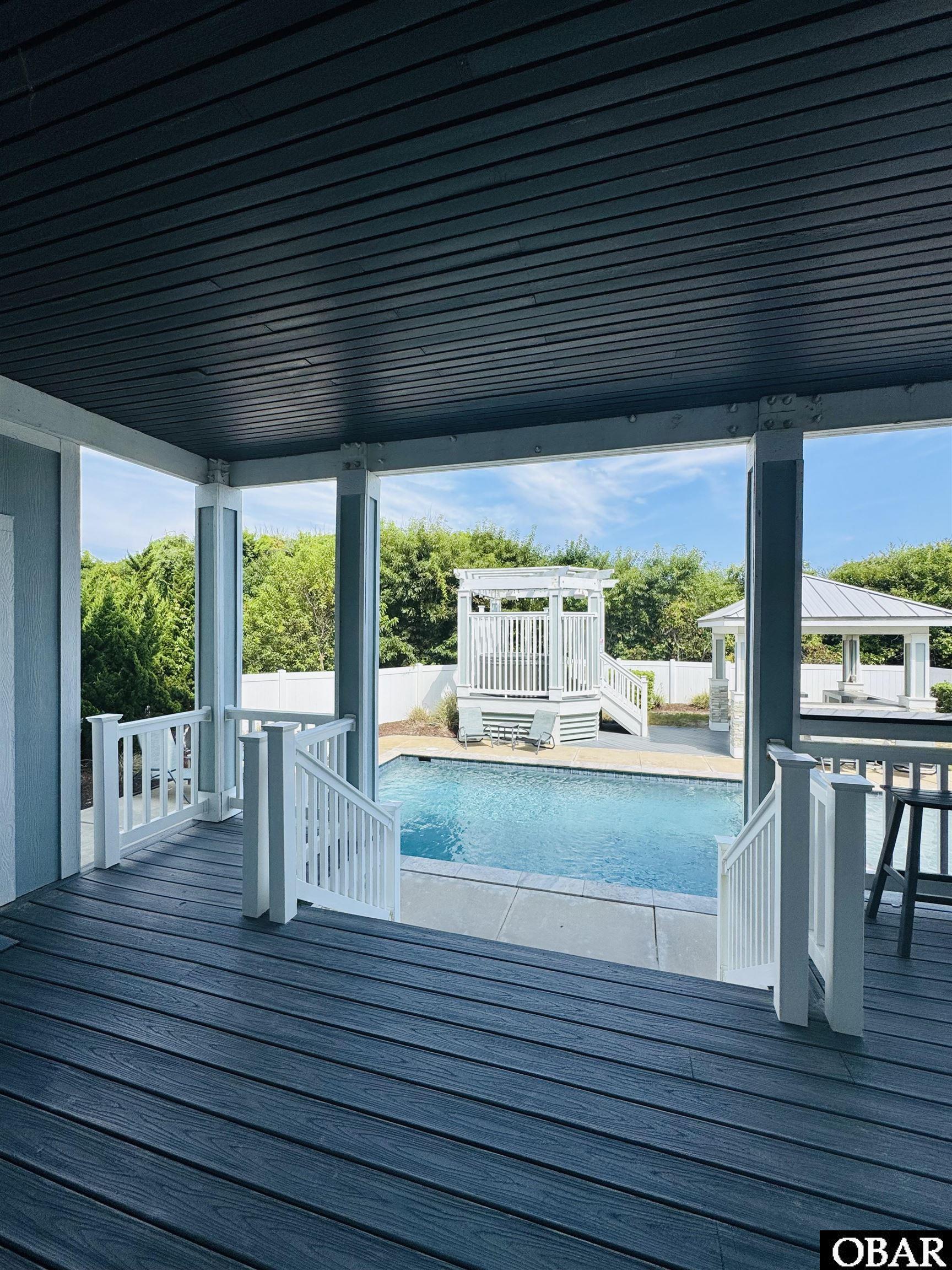 Covered deck overlooking a swimming pool, raised pavilion, and poolside gazebo.