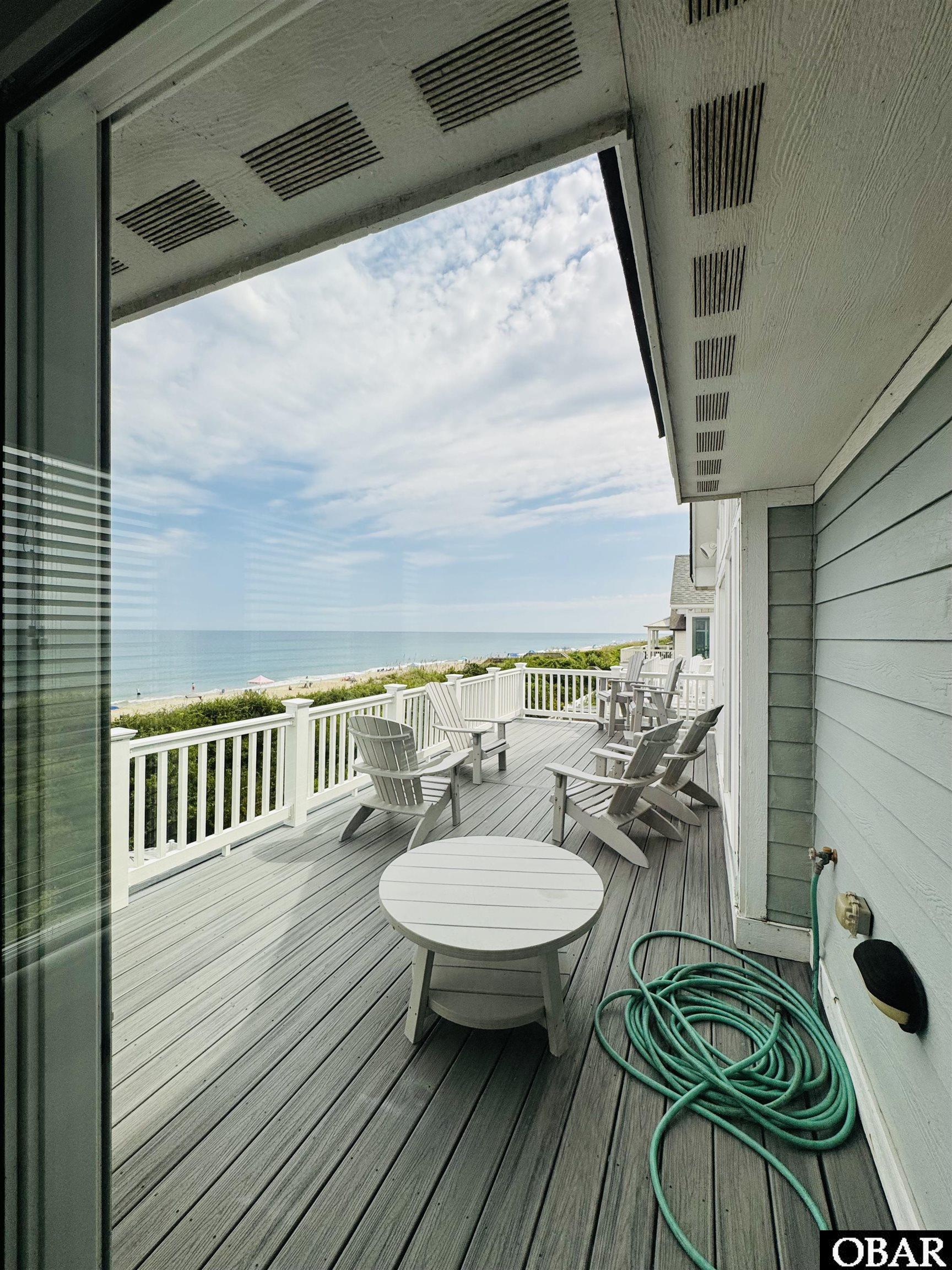 Seaside deck with Adirondack chairs and a round table overlooking the beach and ocean.