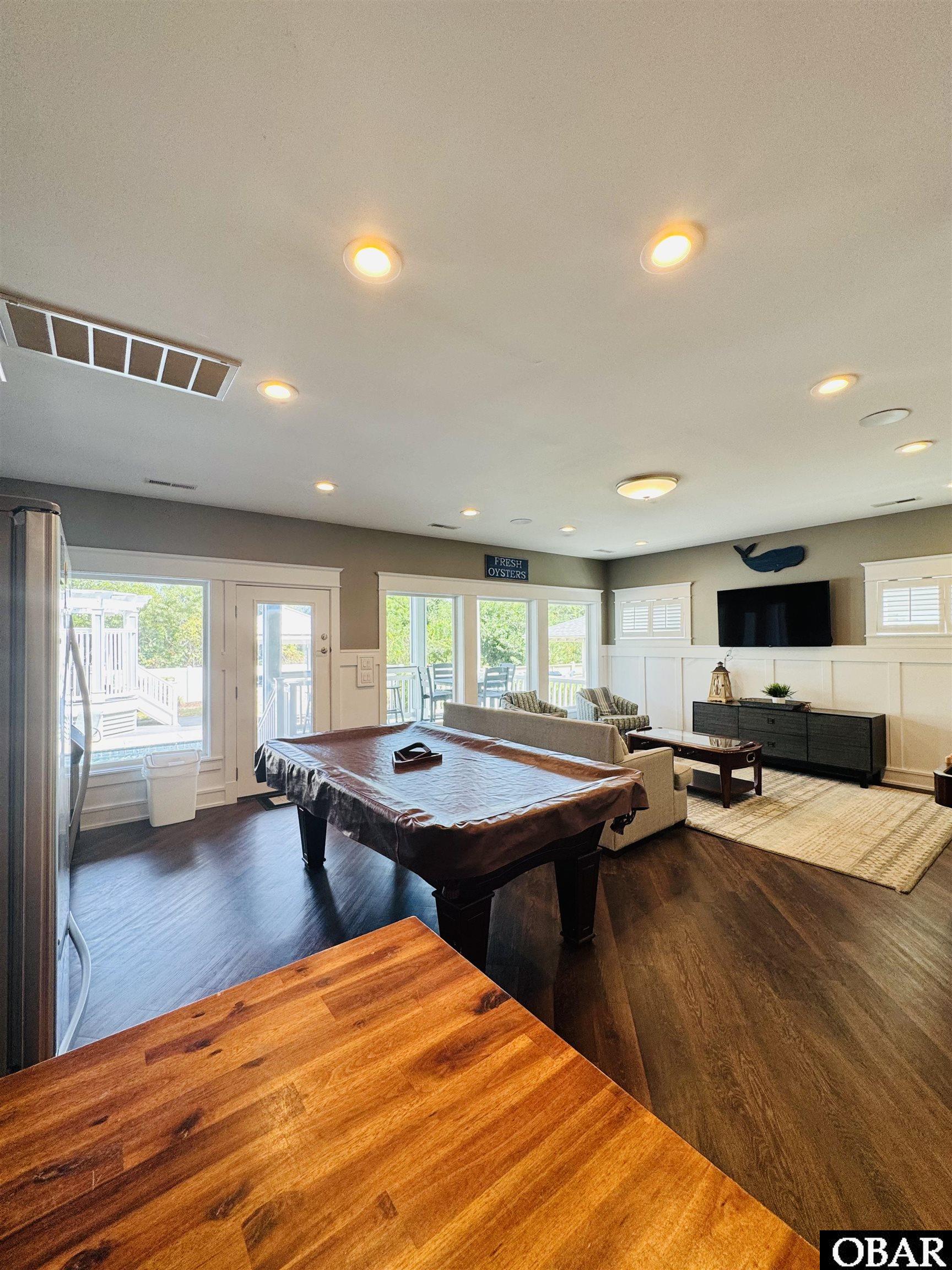 Game room with a pool table, sofa seating, and television beside windows overlooking a deck.