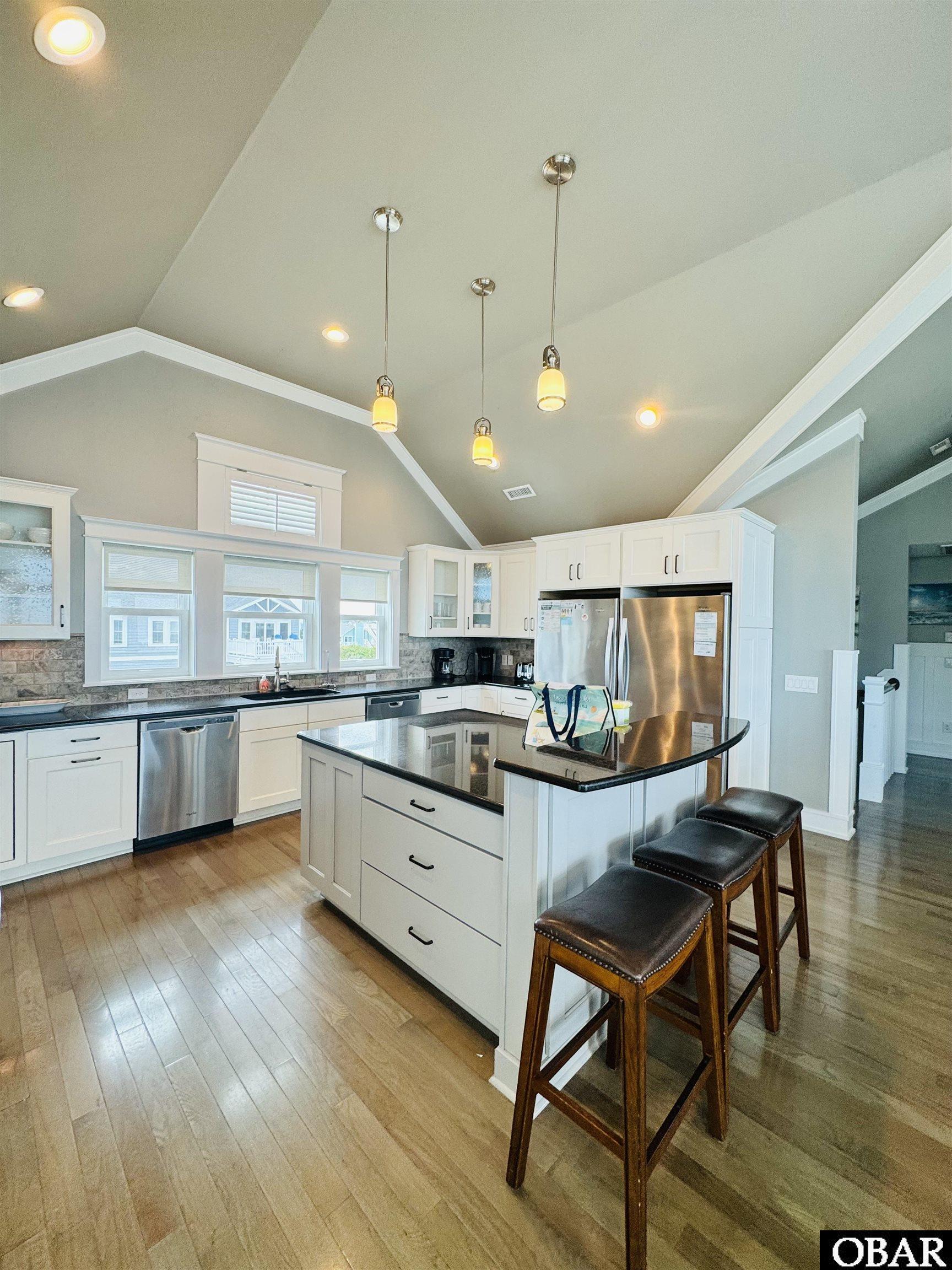 Kitchen with a black-topped island, three bar stools, white cabinets, and a vaulted ceiling.