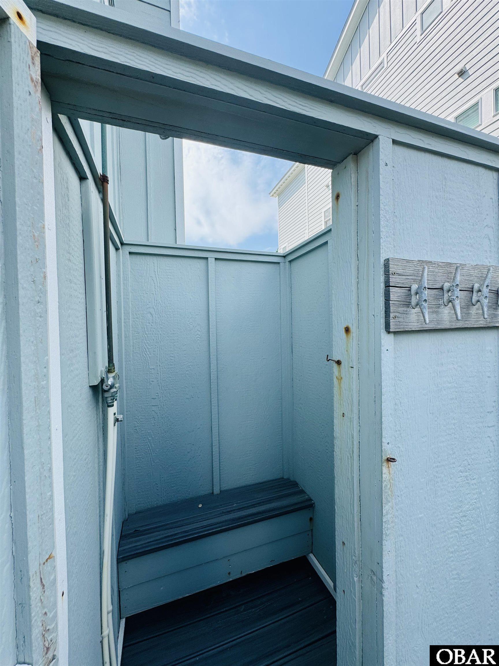 Outdoor shower with a built-in bench, pale blue wooden enclosure, and wall hooks.
