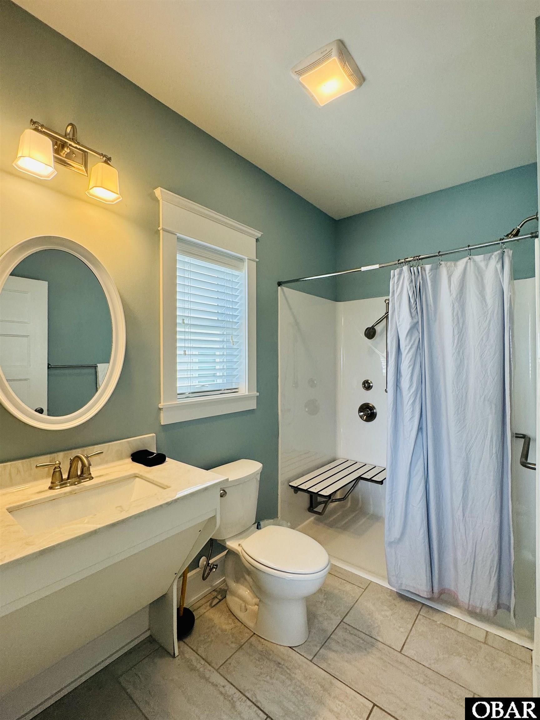 Bathroom with teal walls, white vanity, oval mirror, and walk-in shower with a folding seat.