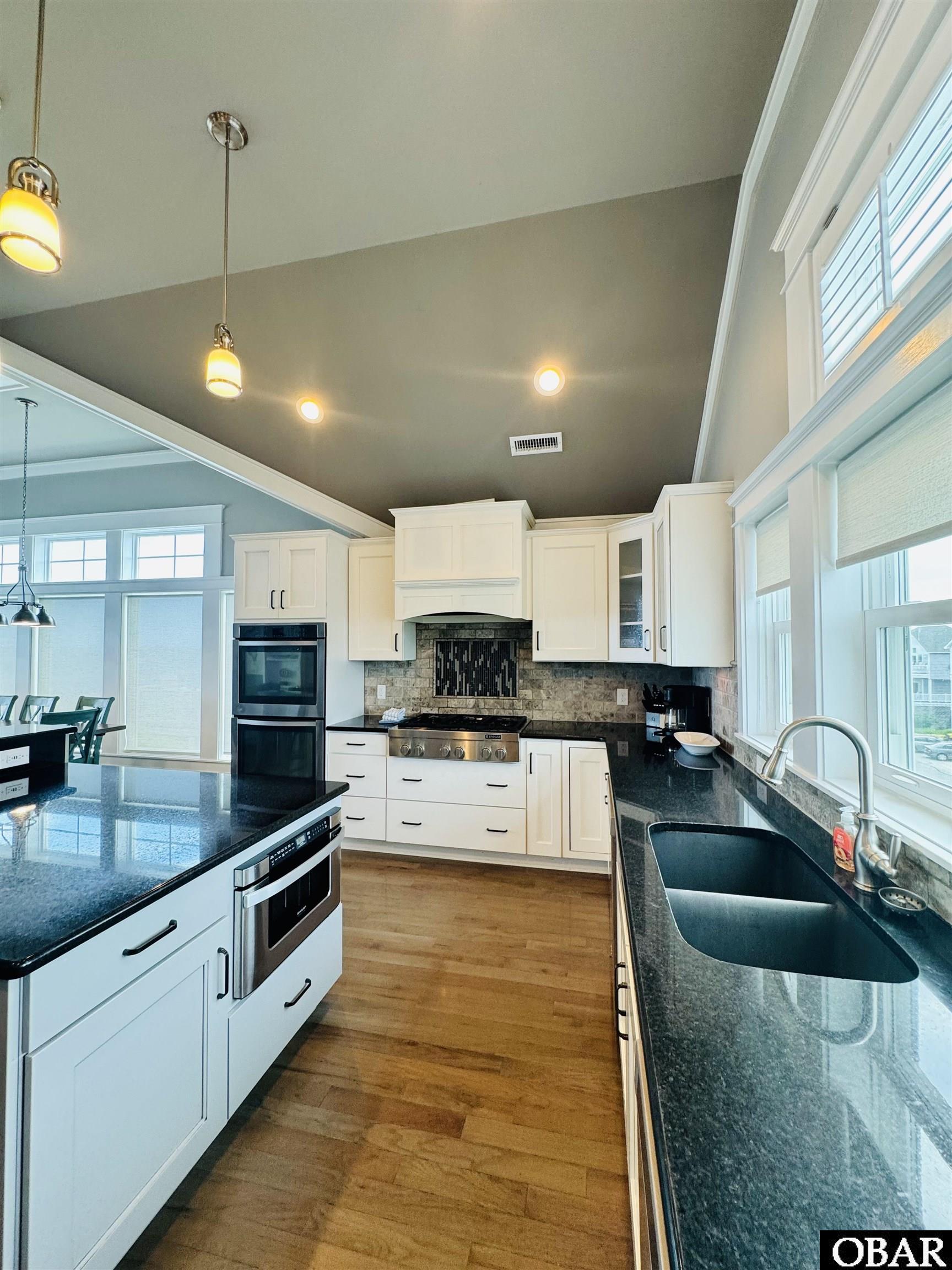 Kitchen with white cabinetry, dark granite counters, stainless steel appliances, and tall windows.