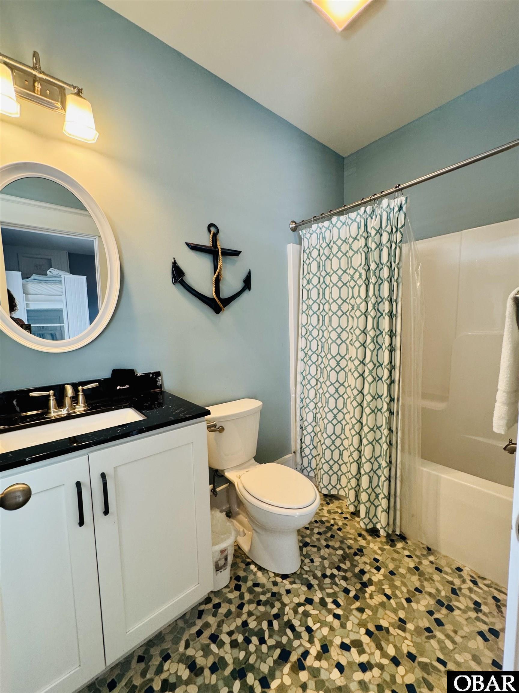 Bathroom with teal walls, anchor decor, patterned shower curtain, and multicolored pebble floor tile.