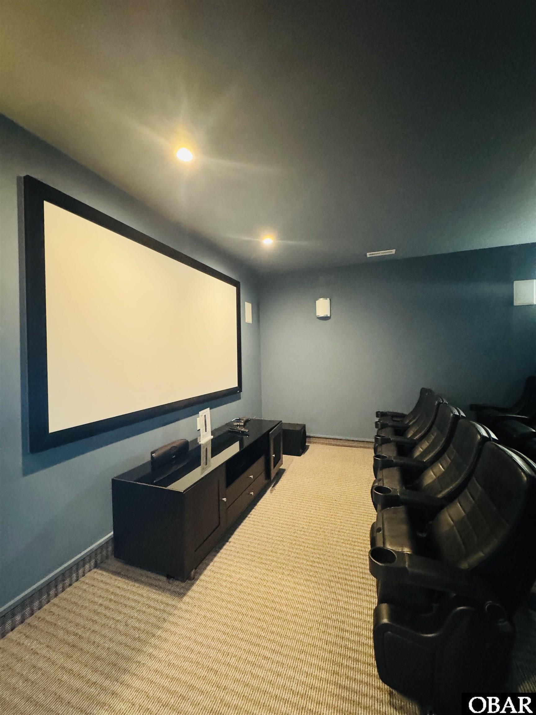 Home theater with a large projection screen and a row of black leather recliners.