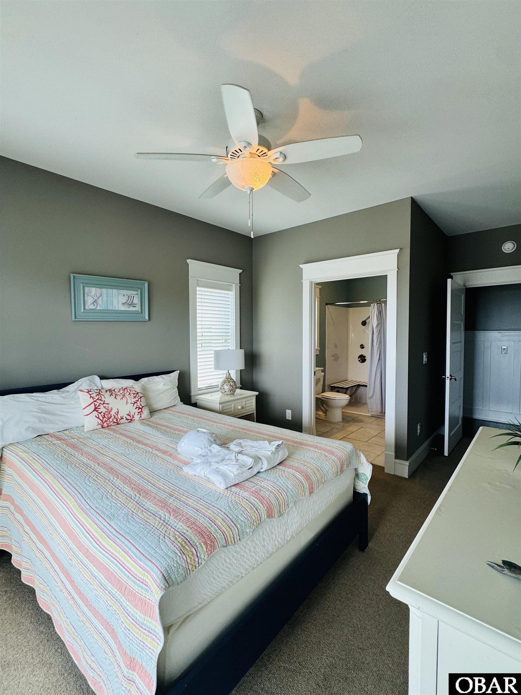 Bedroom with pastel-striped bedding, ceiling fan, and an open doorway to the adjoining bathroom.