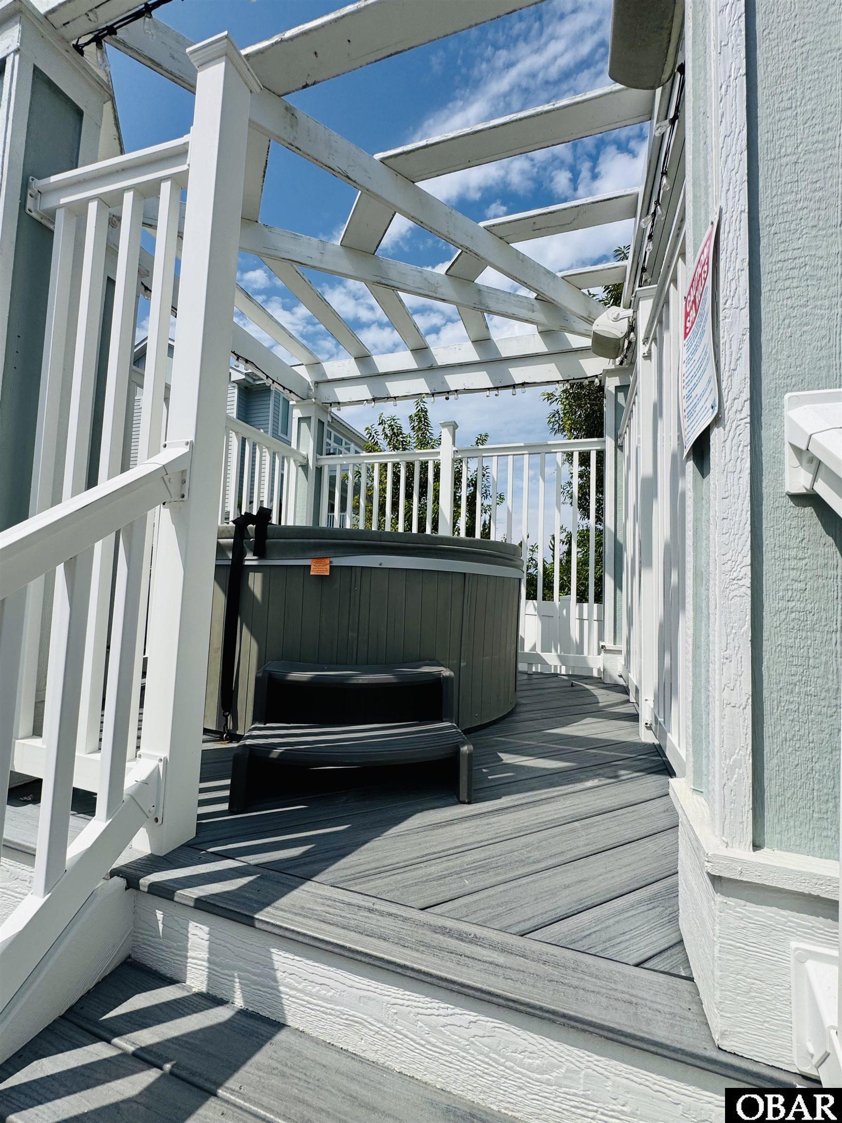 Outdoor deck with a round hot tub beneath a white pergola.