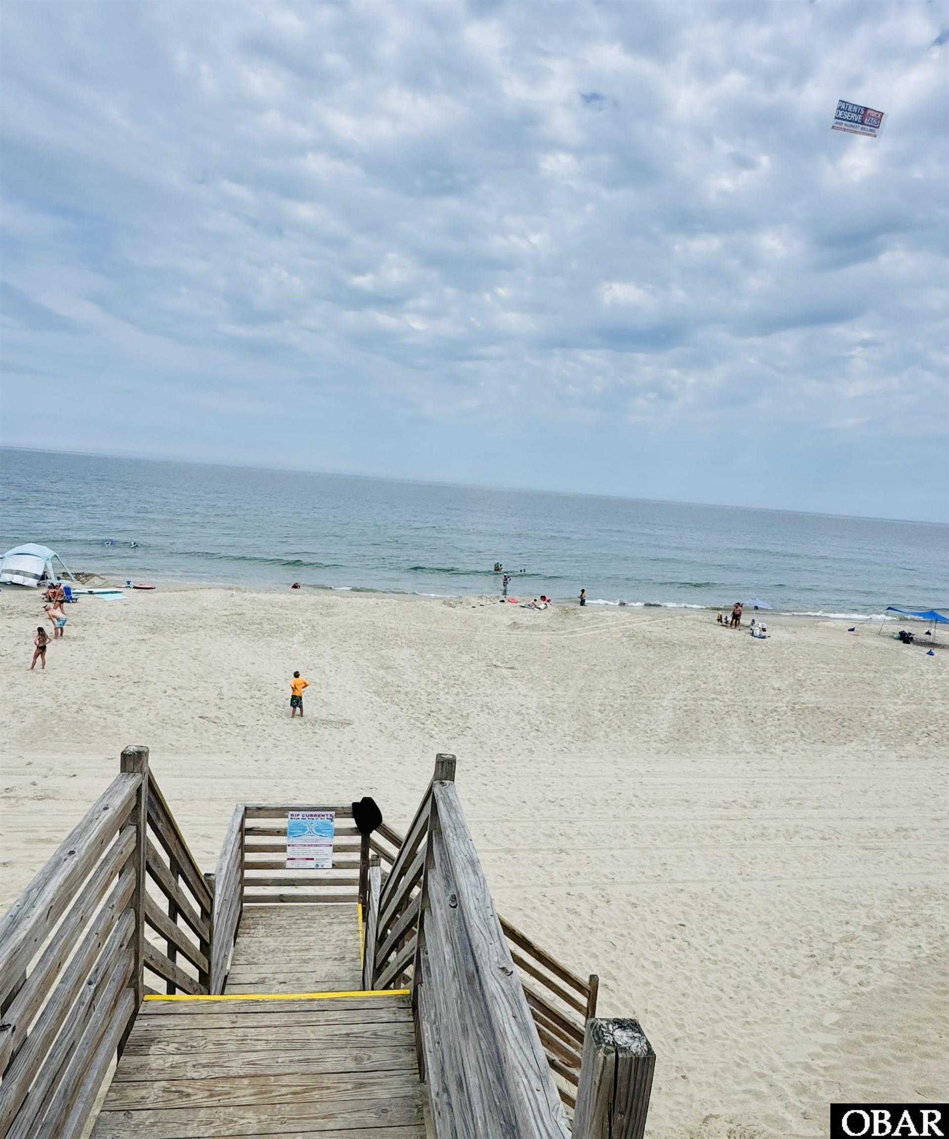 Beach access stairs lead down to a sandy, lightly populated beach and ocean.