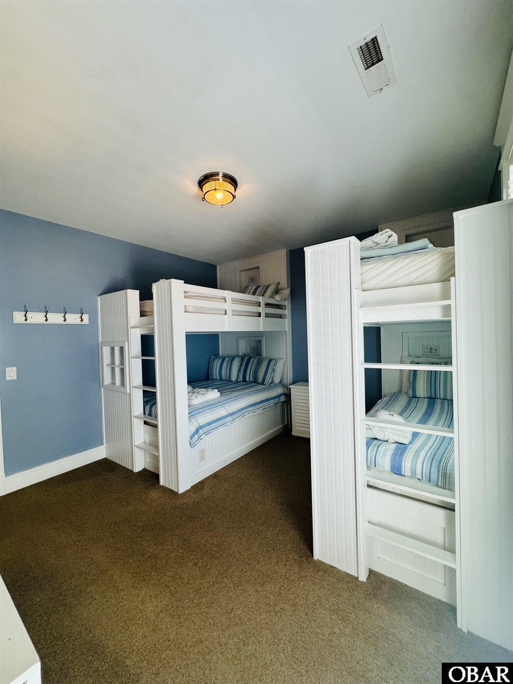 Bedroom with white bunk beds, blue striped bedding, blue walls, and brown carpet.