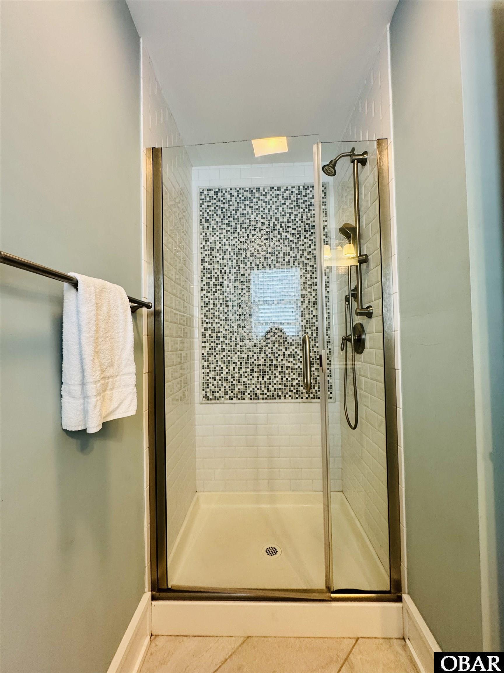 Walk-in shower with glass doors, a black-and-white mosaic accent wall, and white tile.