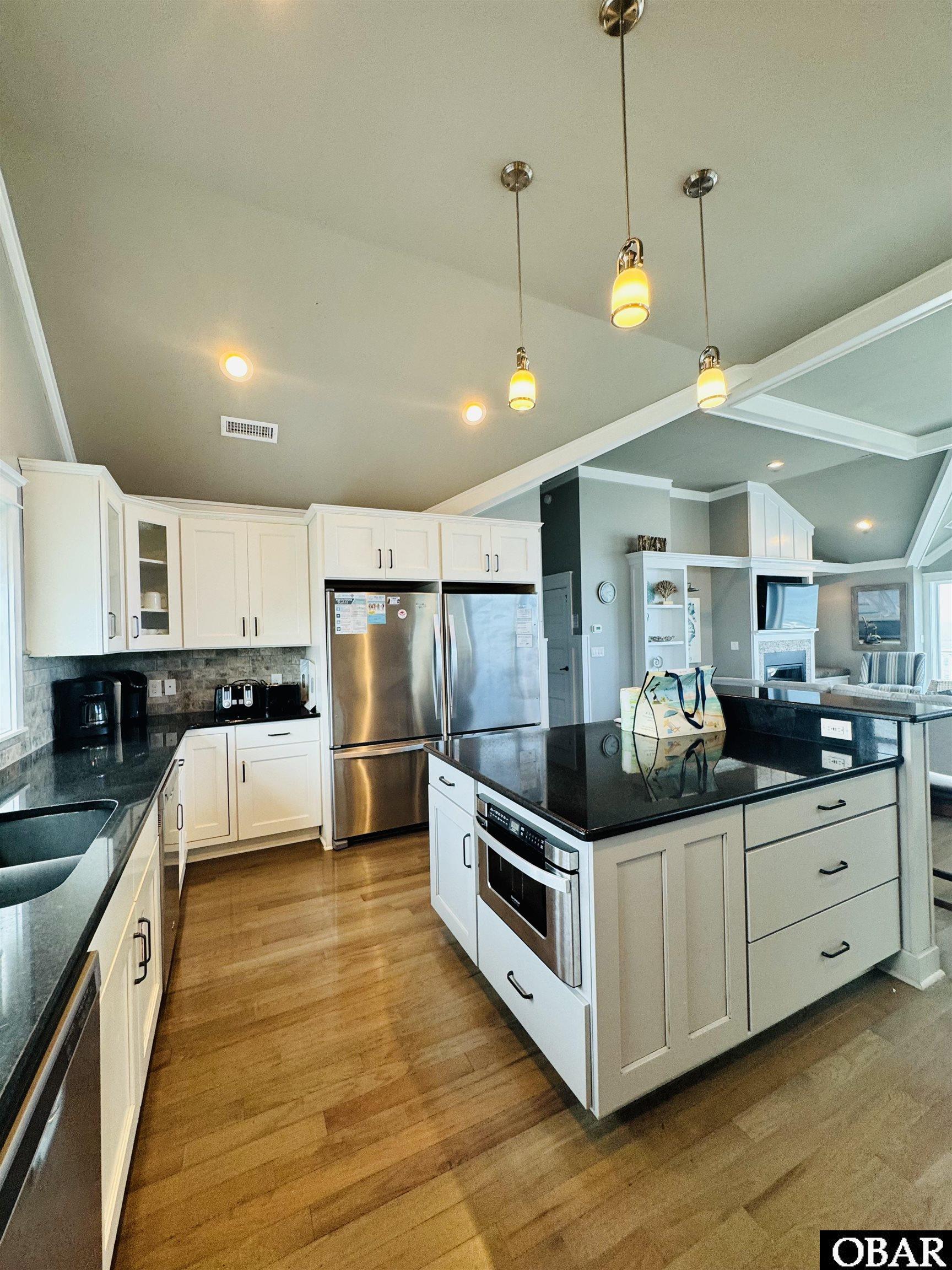 Kitchen with a large dark-countertop island, white cabinetry, and stainless steel appliances.