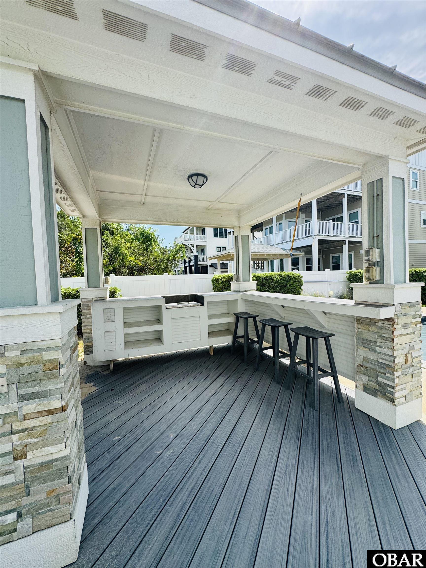Covered porch with a built-in bar, three black stools, and stone-clad columns.