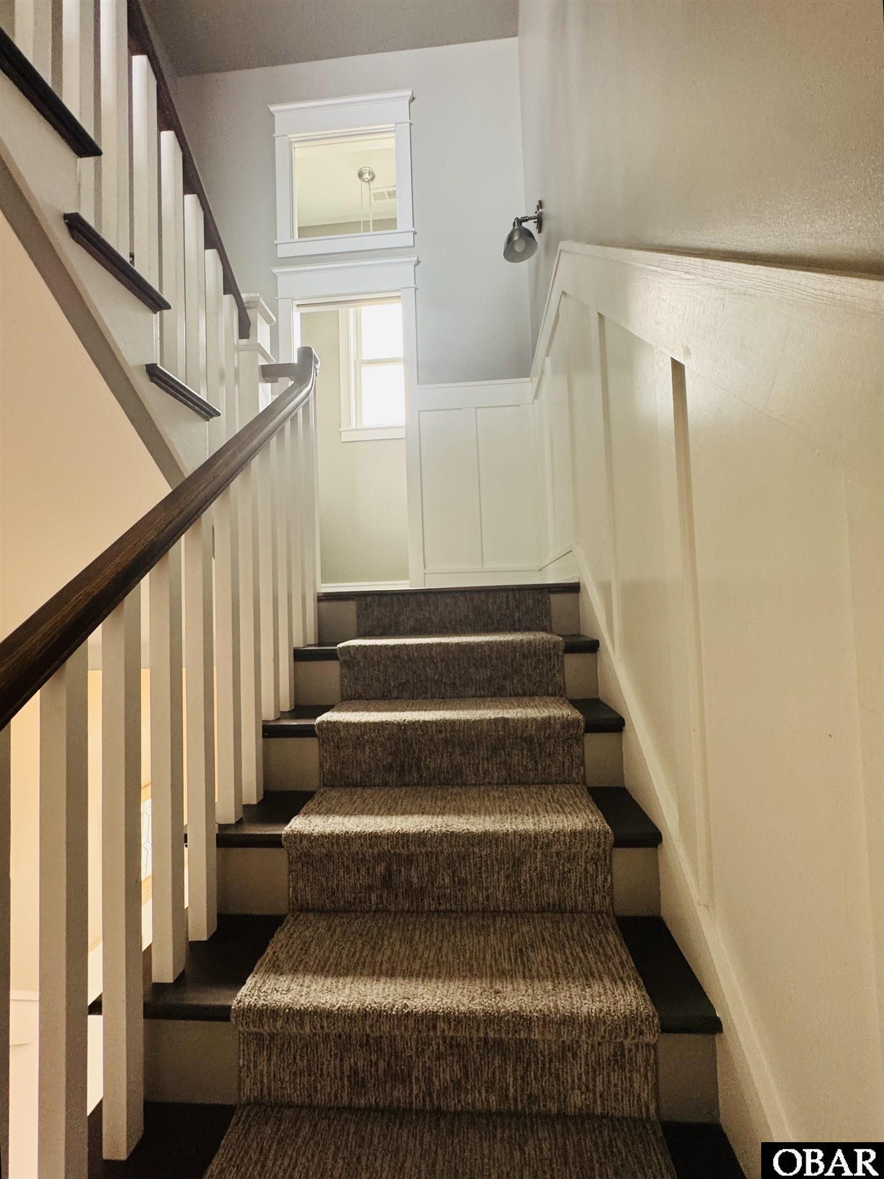 Carpeted staircase with dark wood treads, white balusters, and a bright window at the landing.