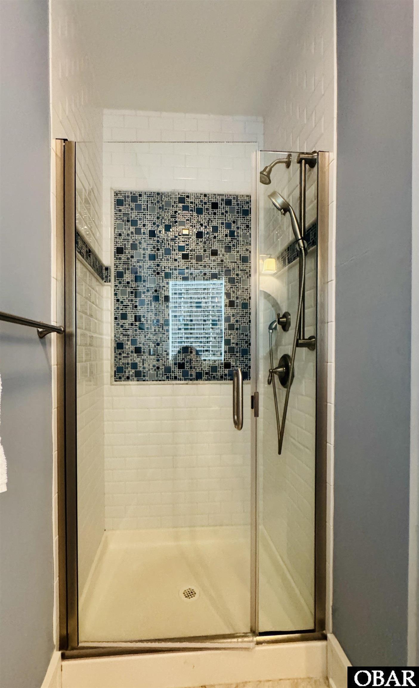 Walk-in shower with a blue geometric mosaic accent wall, glass enclosure, and handheld showerhead.