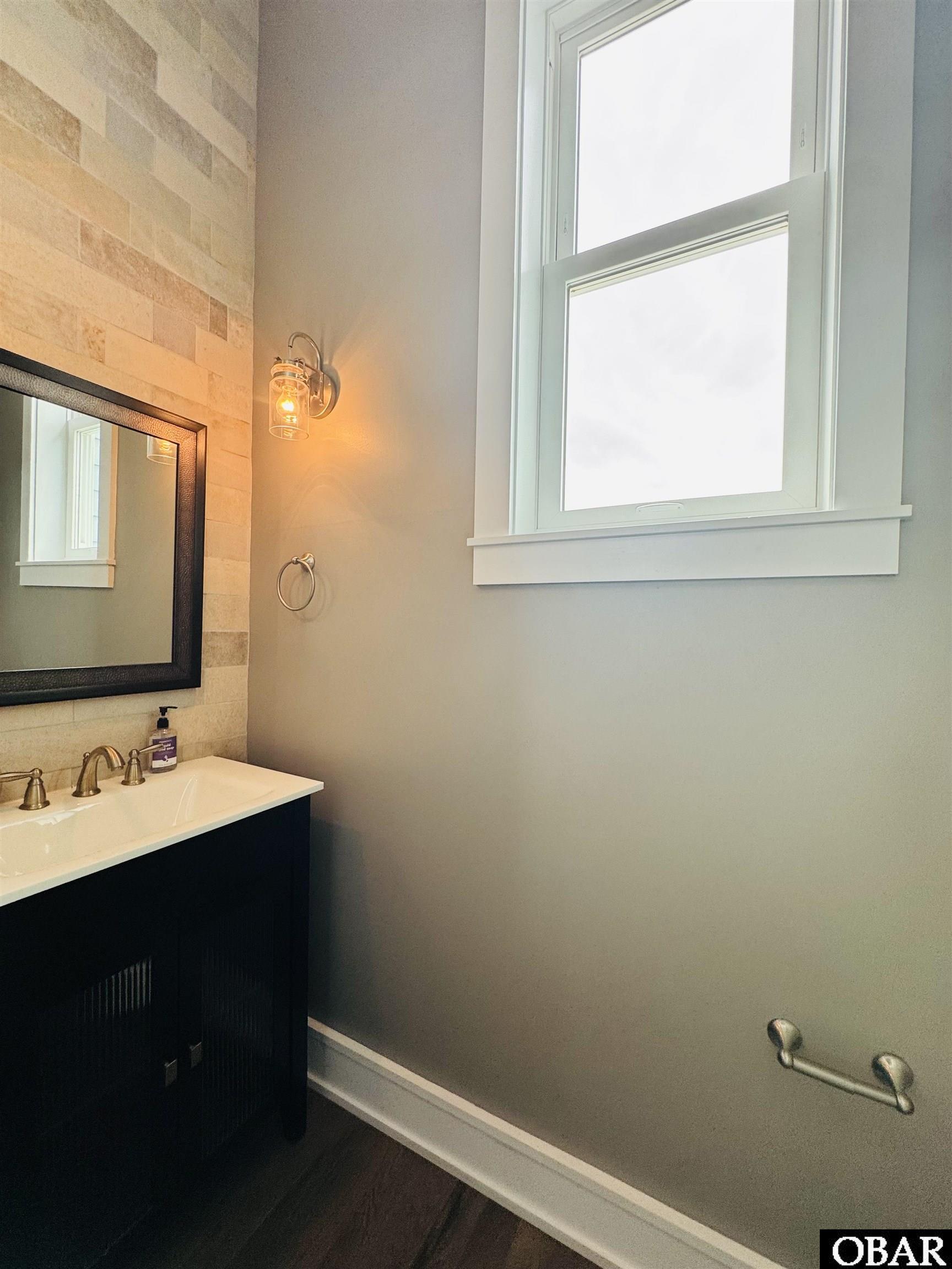 Bathroom vanity with beige stone tile, a large window, and a lit wall sconce.