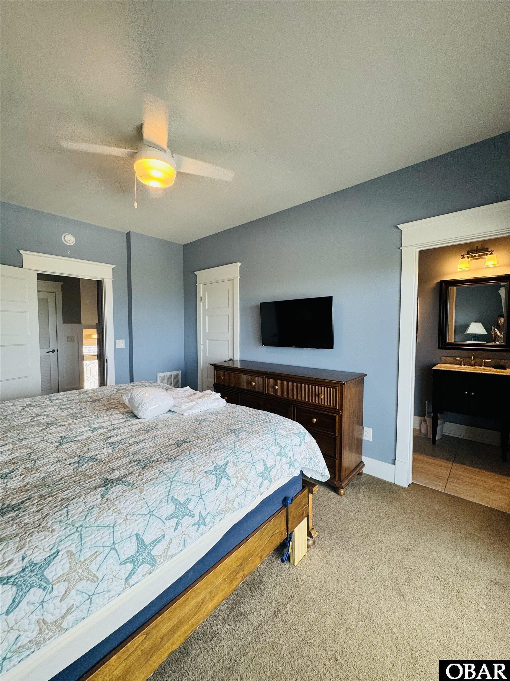 Bedroom with a starfish-patterned bedspread, wooden dresser, wall-mounted TV, and adjoining bathroom.