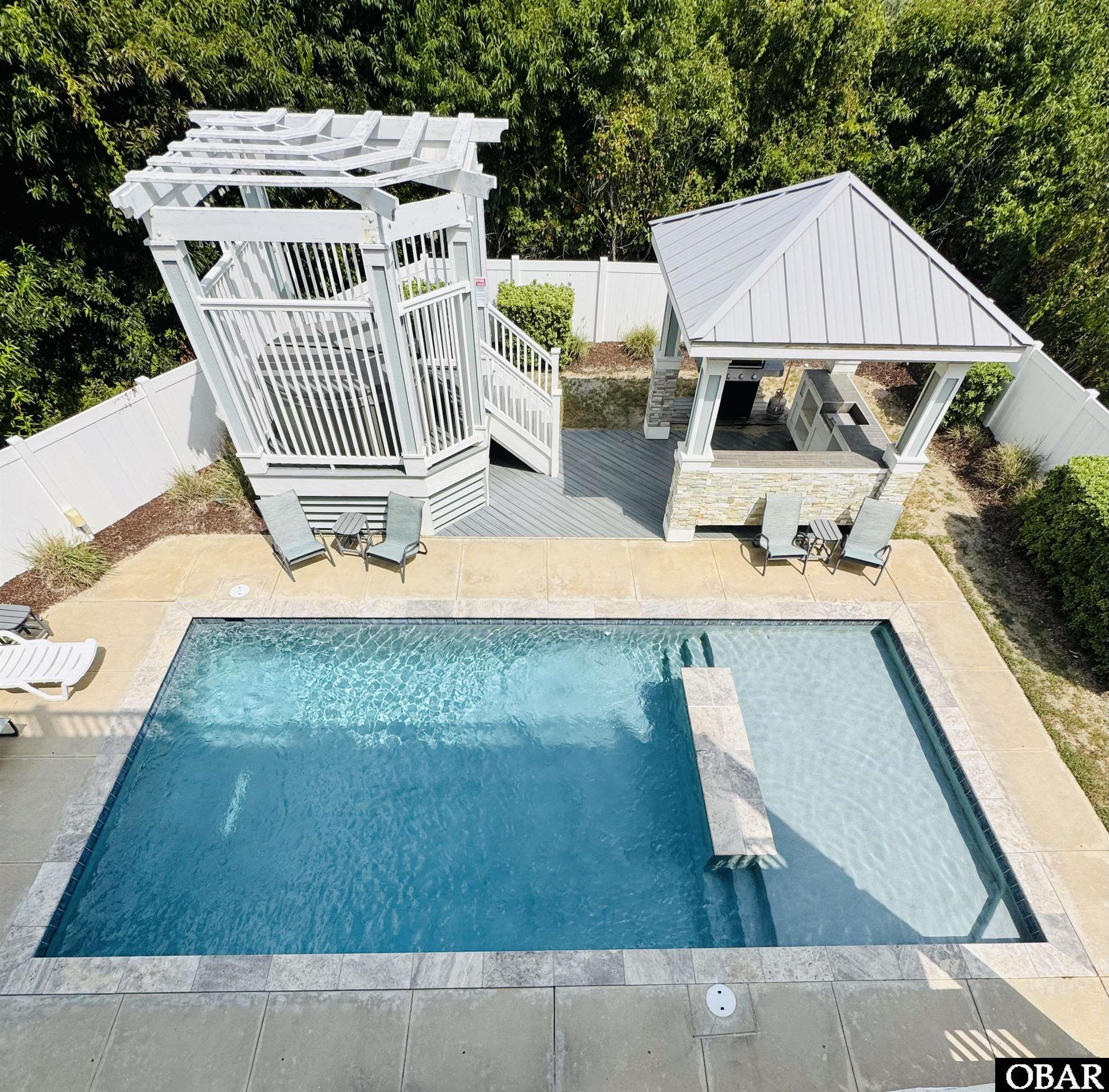 Aerial view of the pool, shallow sun shelf, white pergola, and covered outdoor kitchen.