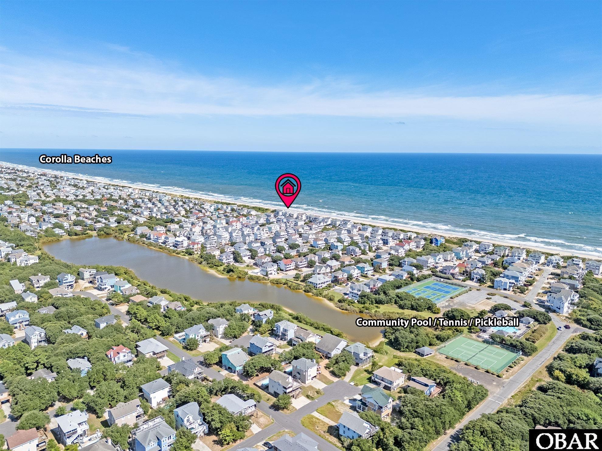 Aerial view of Corolla beach community, oceanfront homes, and community pool, tennis, and pickleball courts.