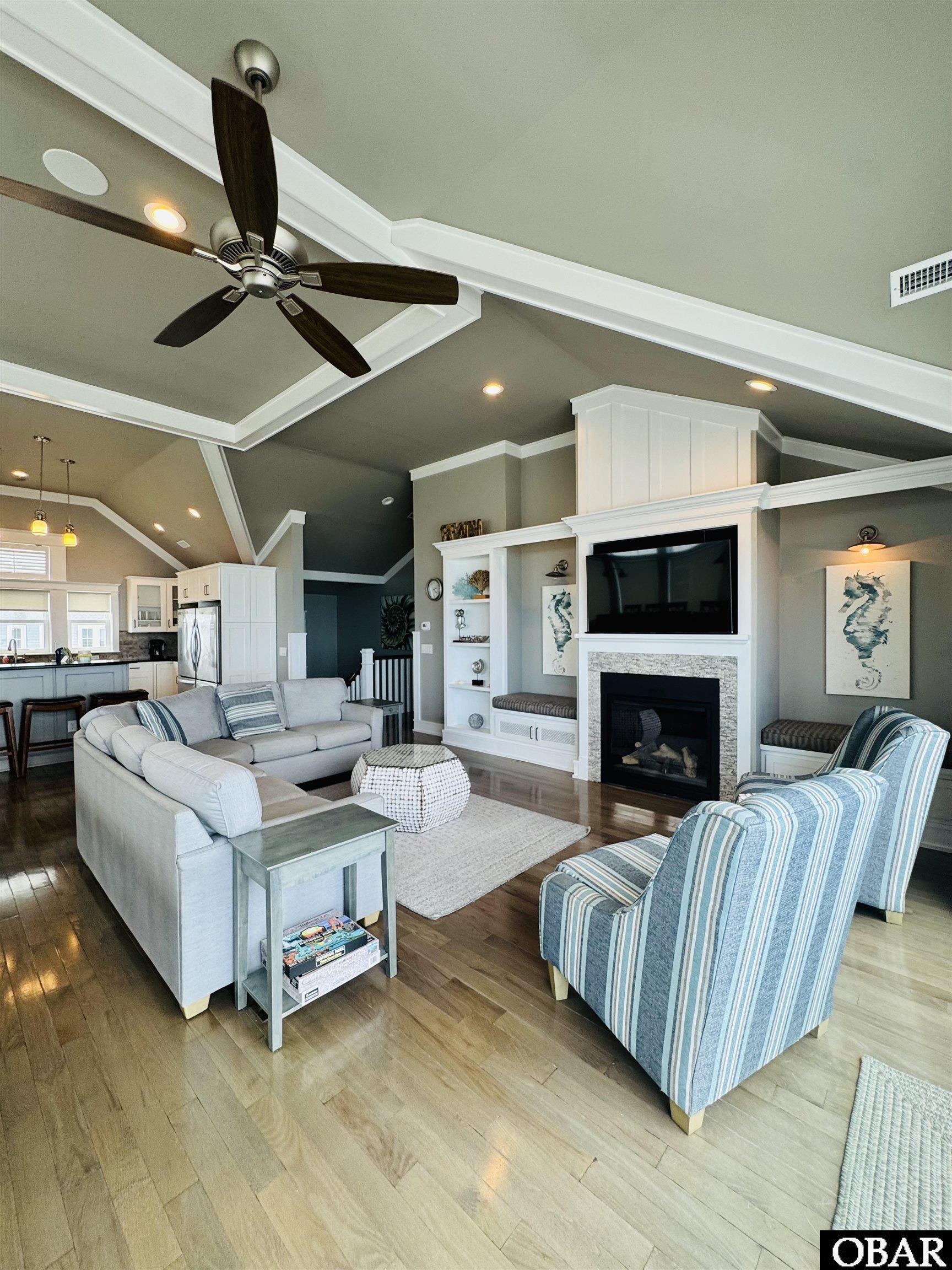 Living room with vaulted ceiling, fireplace, light sectional sofa, and blue-striped armchairs.