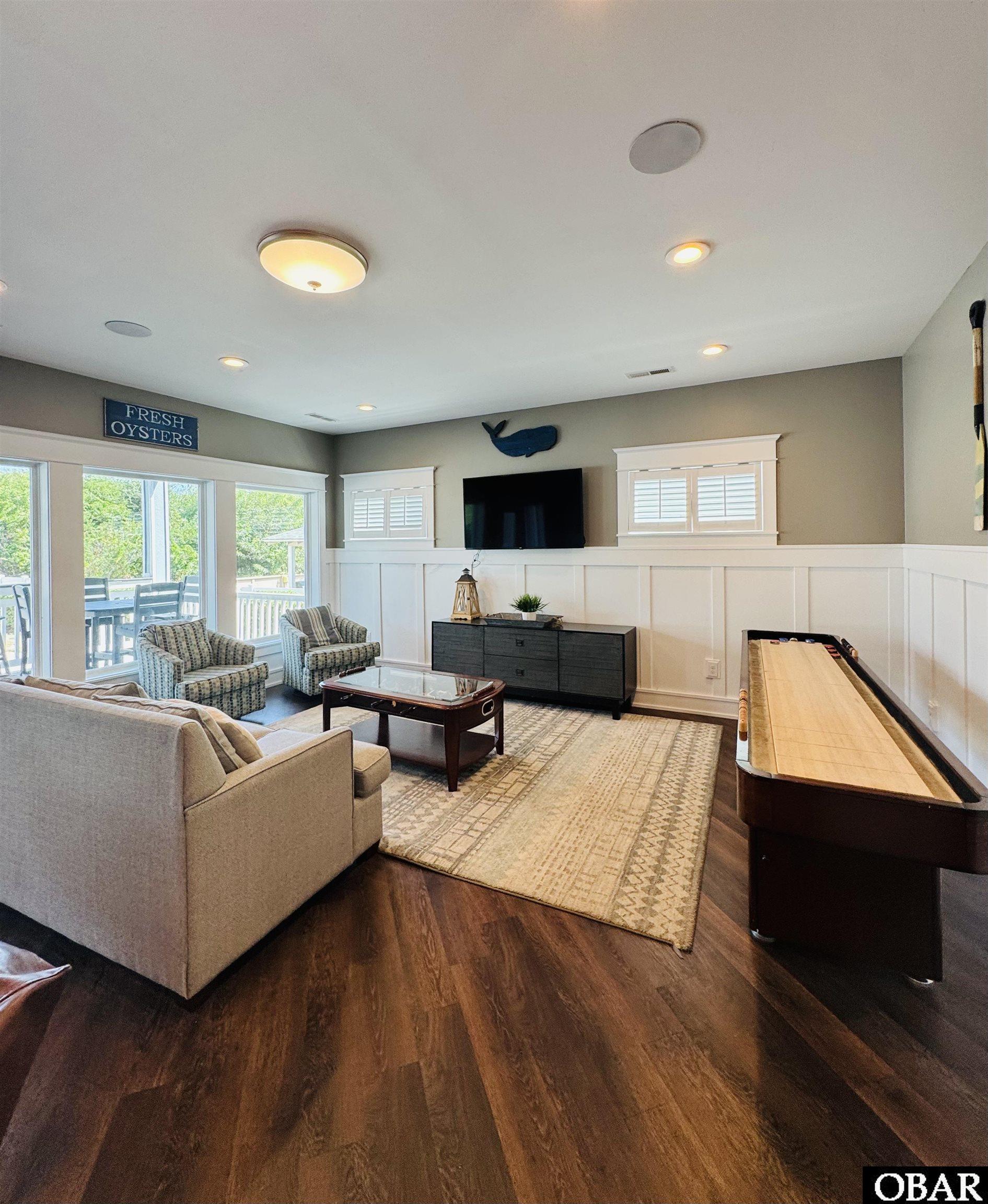 Living and game room with a shuffleboard table, shuttered windows, and seating area.
