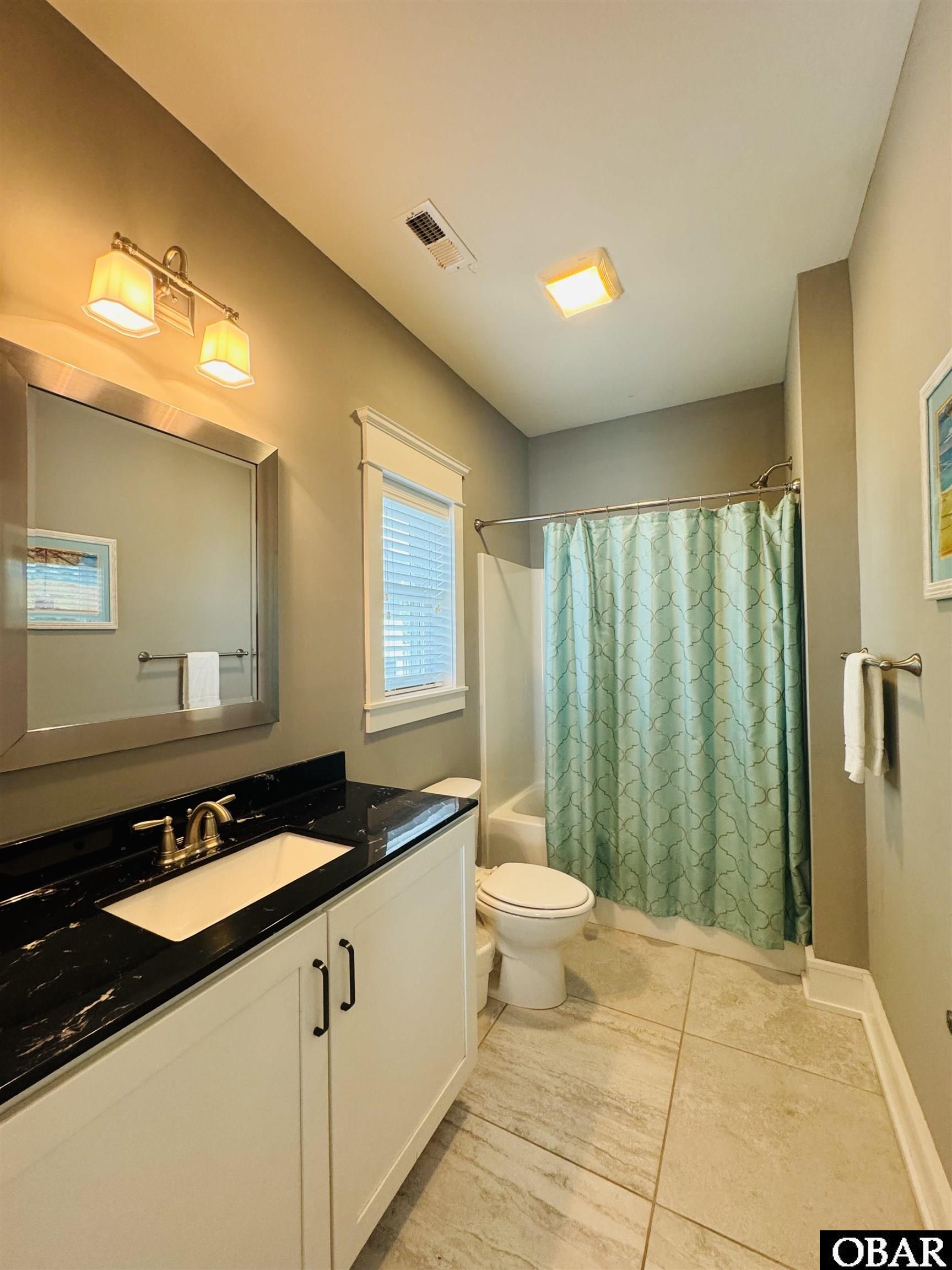 Bathroom with a black countertop vanity, aqua shower curtain, and beige tile floor.