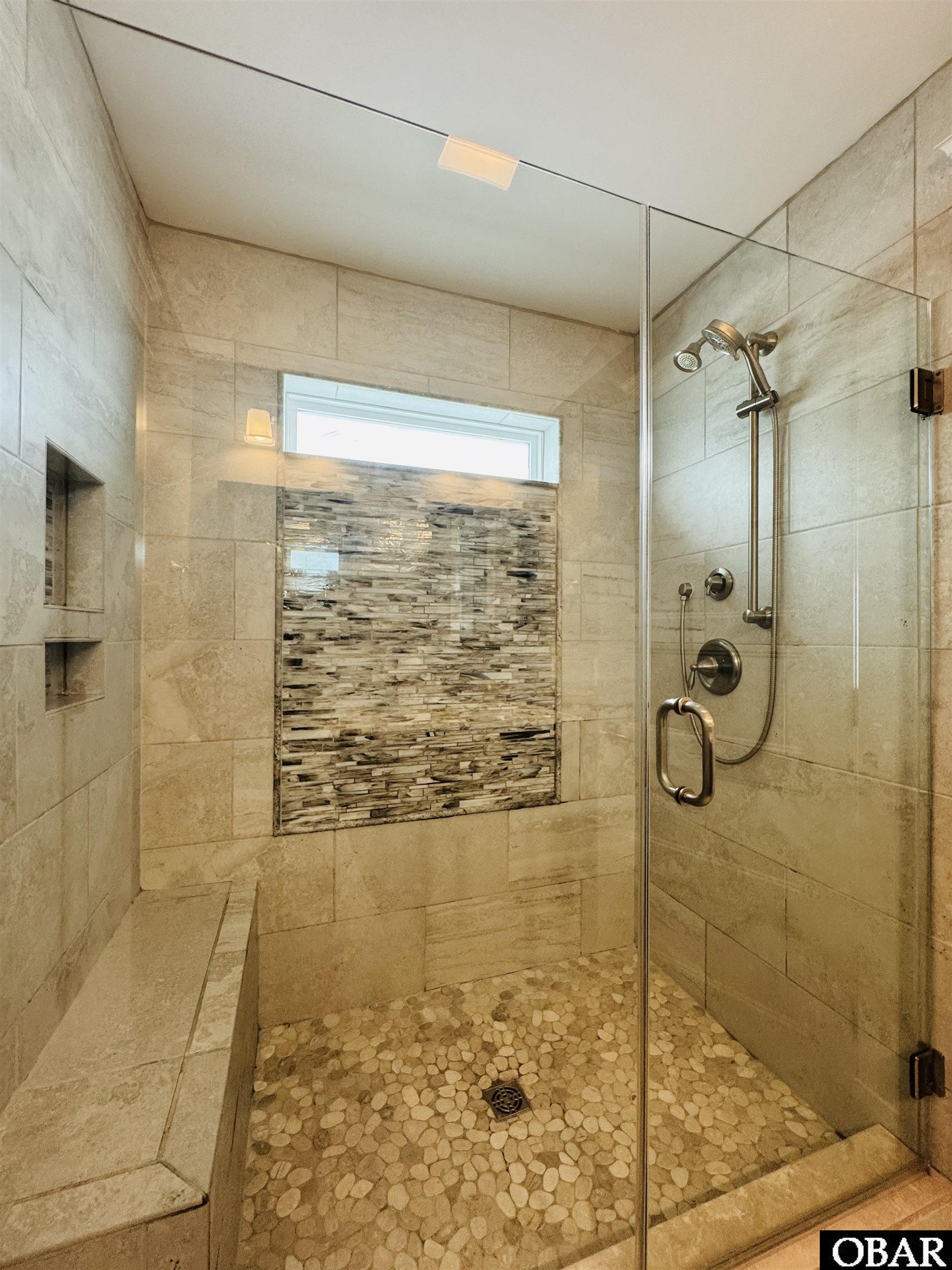 Walk-in shower with pebble flooring, mosaic accent wall, built-in niches, and a tiled bench.