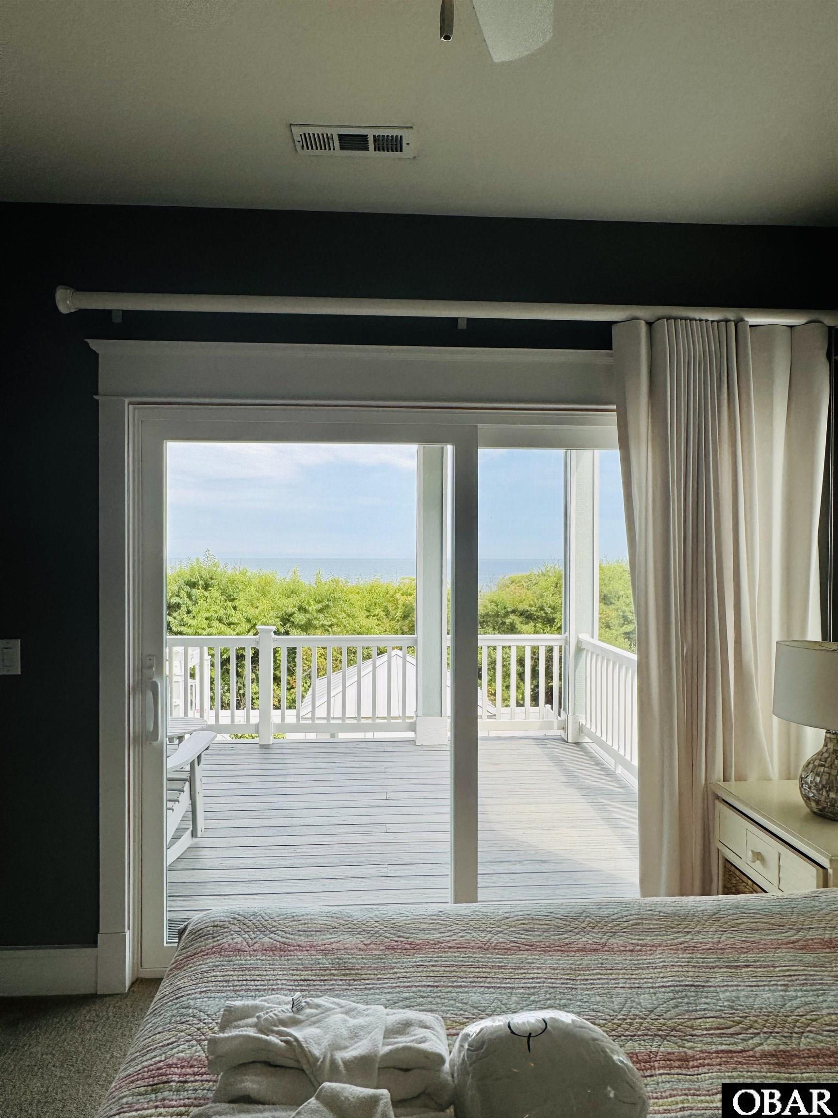 Bedroom with sliding doors to a white-railed deck and ocean view.
