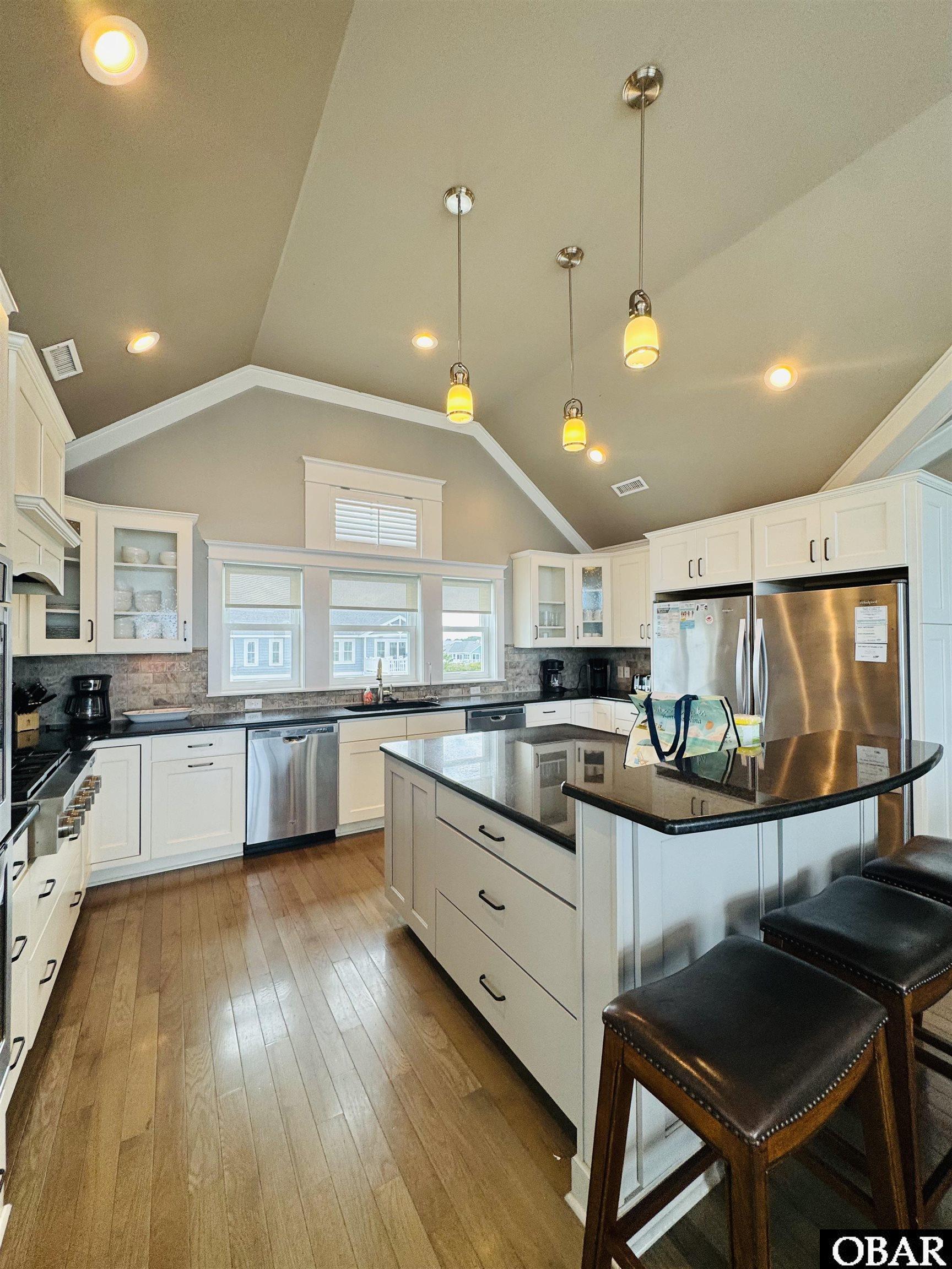 Kitchen with a large island, white cabinetry, stainless steel appliances, and vaulted ceiling.